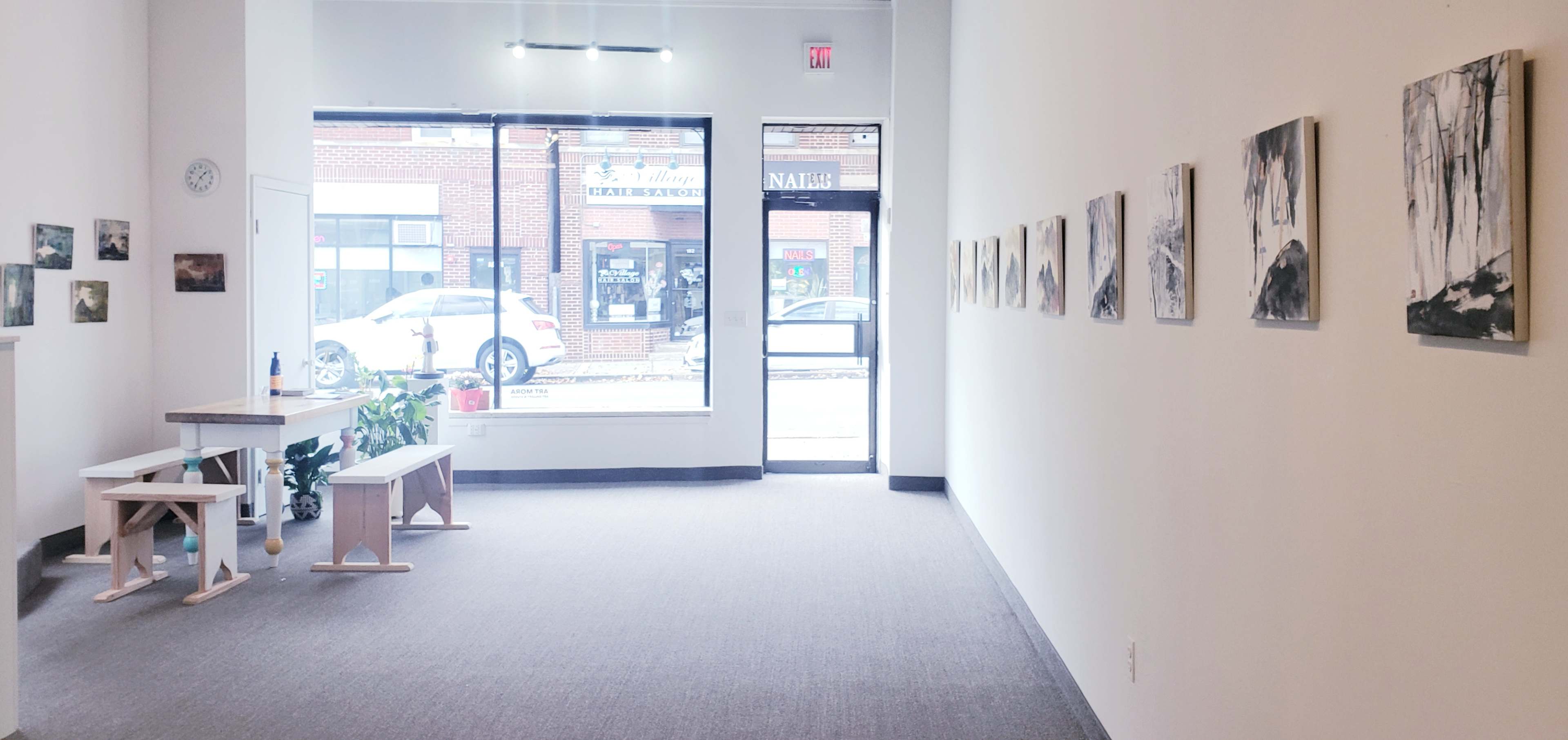 A spacious art gallery features a series of black-and-white artworks displayed on the walls, with a bench and a small table positioned in the center.