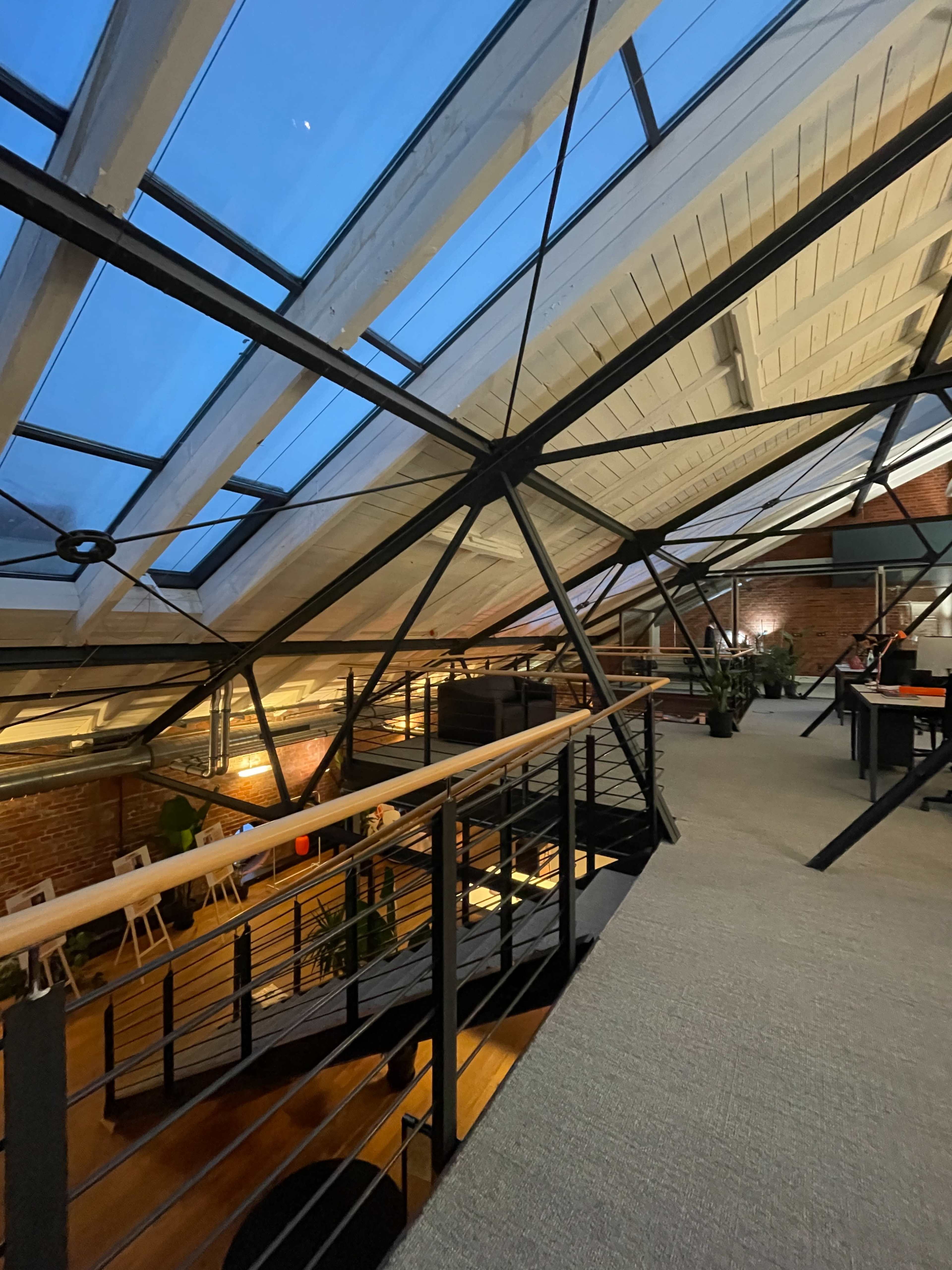 The image shows a spacious loft interior with large skylights, industrial beams, and a staircase leading to a lower level.