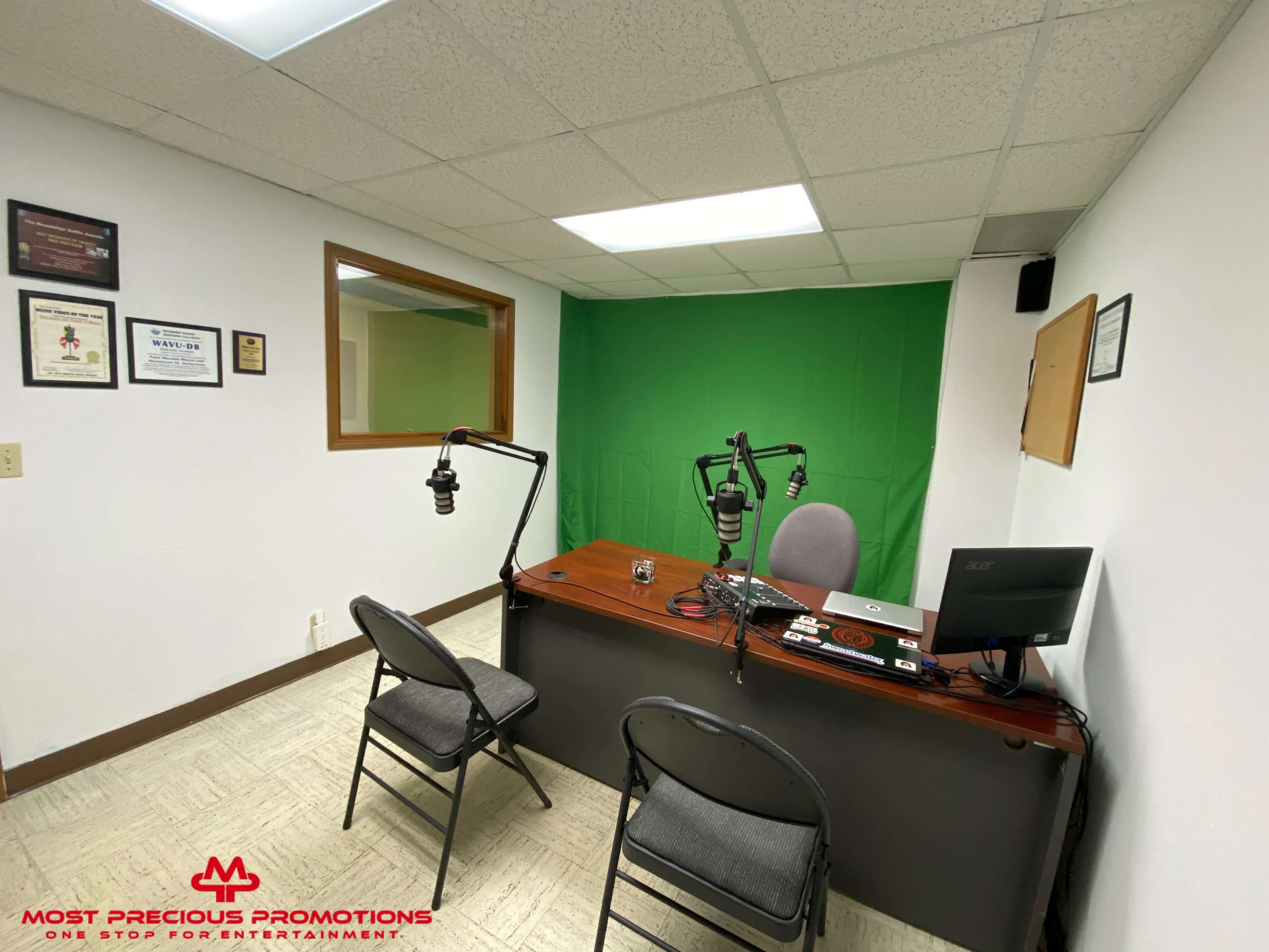 A small recording studio features two chairs, a desk with a computer, and a green screen backdrop.