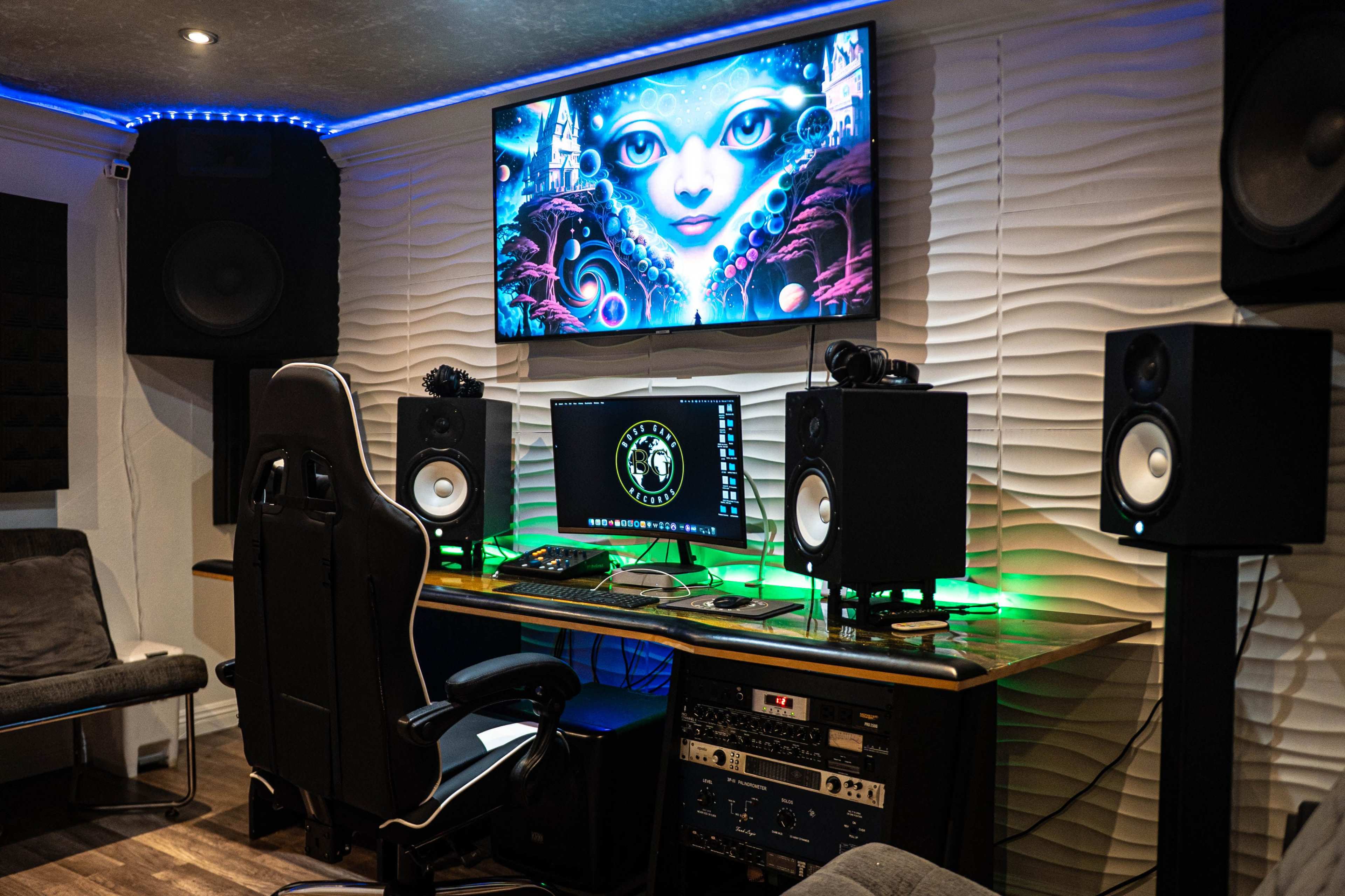 A modern music studio features a workstation with a computer monitor, speakers, and a decorative wall-mounted screen displaying artwork.