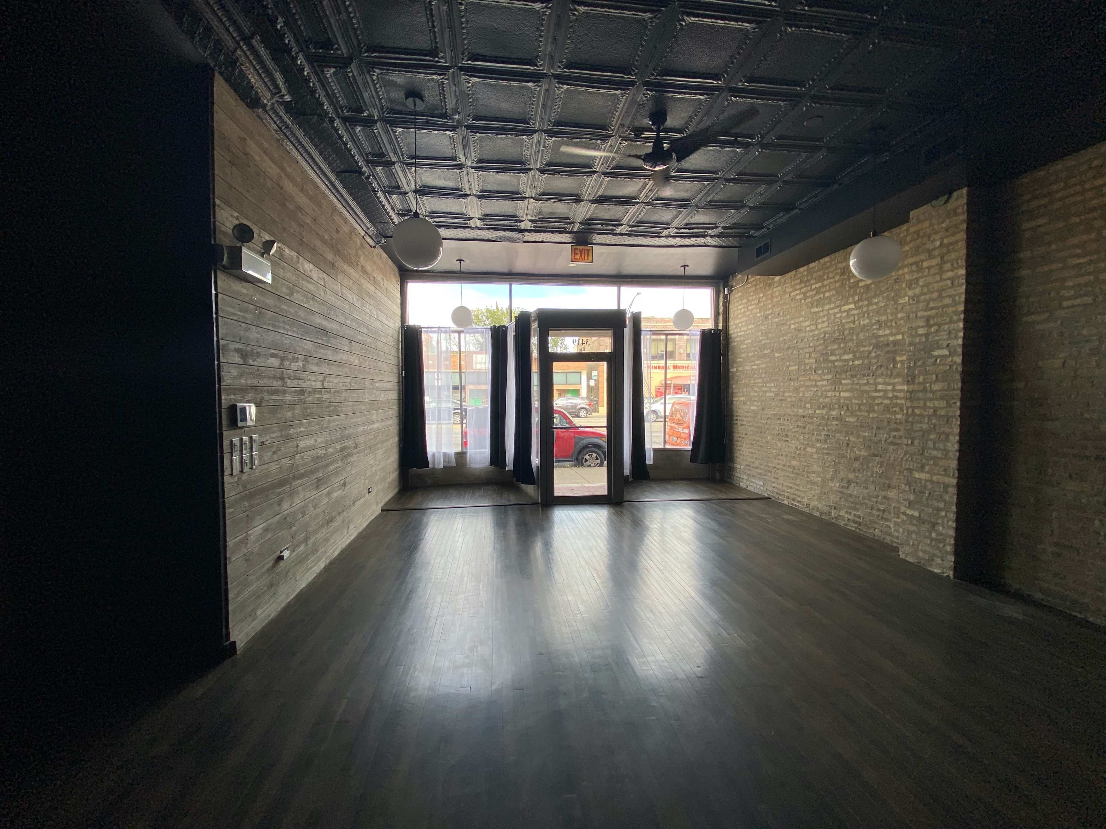 An empty interior space with dark walls, wooden flooring, and large windows at the front.