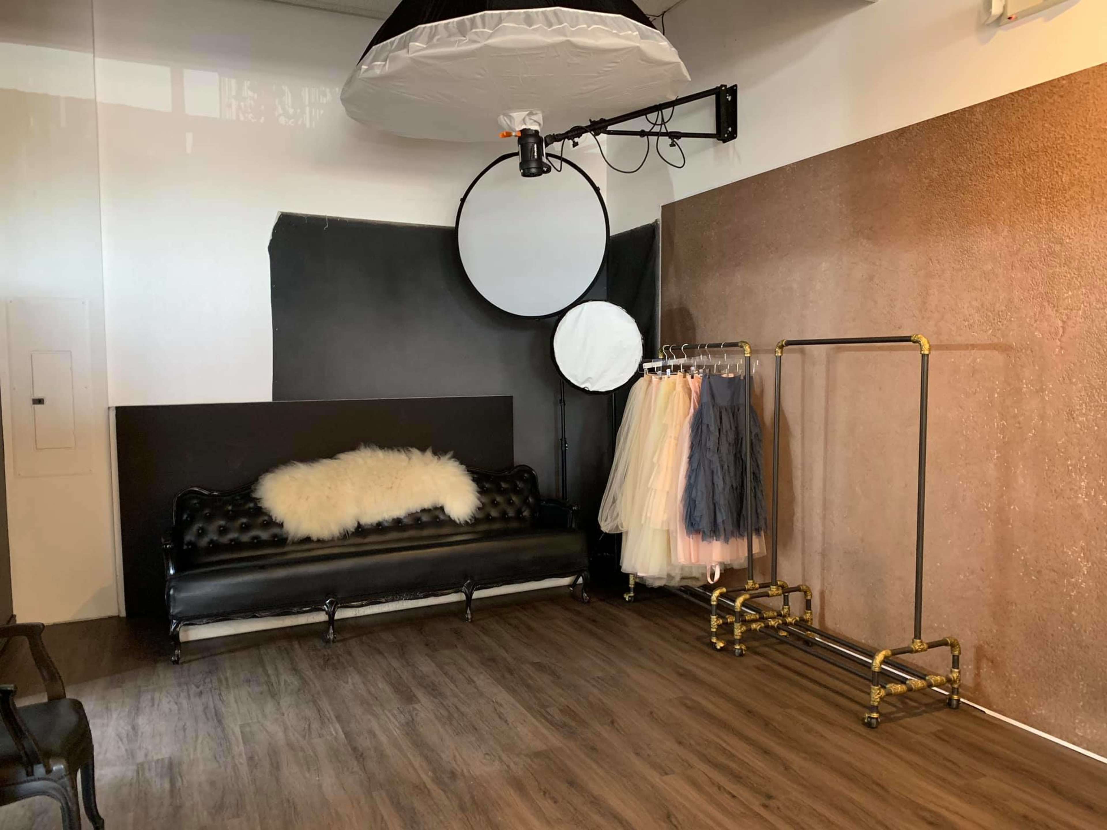 A photo studio featuring a black leather couch, a circular backdrop, and a clothing rack with various pastel-colored garments.