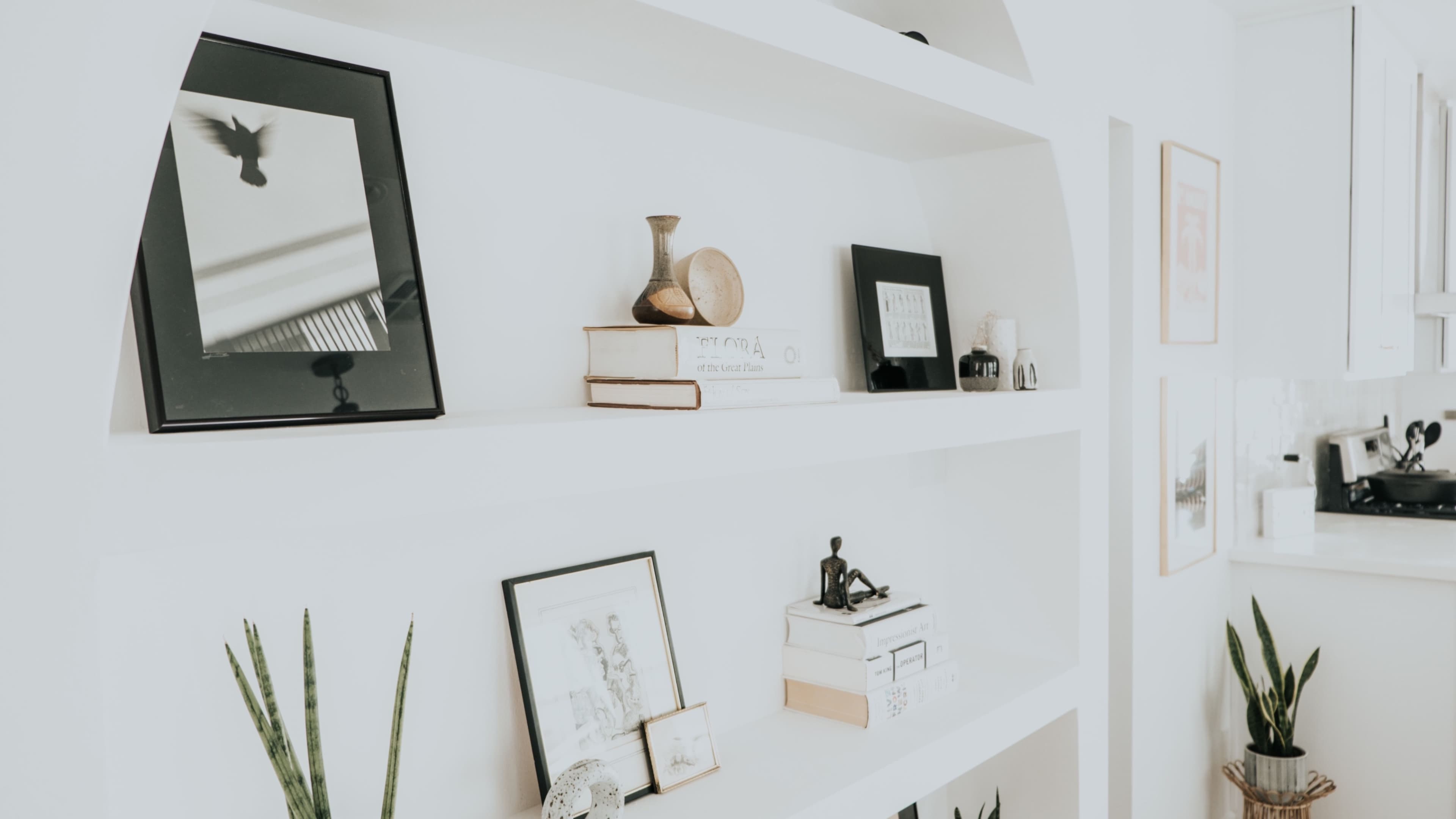 A series of neatly arranged shelves display various framed pictures, decorative objects, and books in a bright environment.