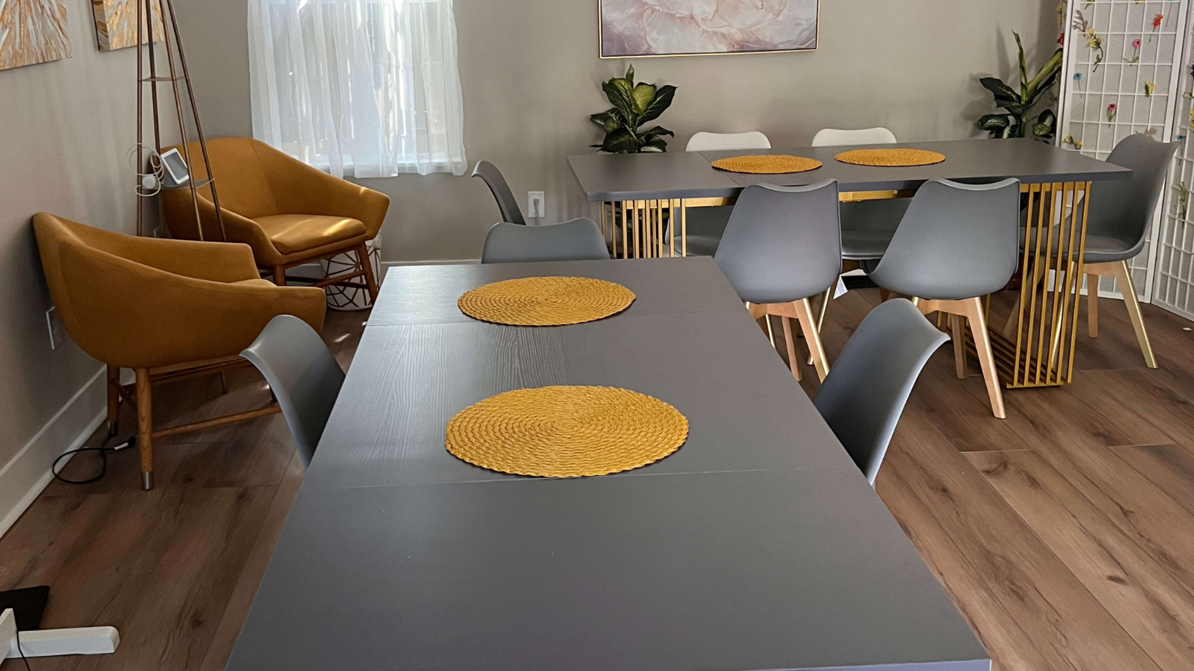 A dining area with two gray tables, chairs, and a yellow accent chair, all set with woven placemats.