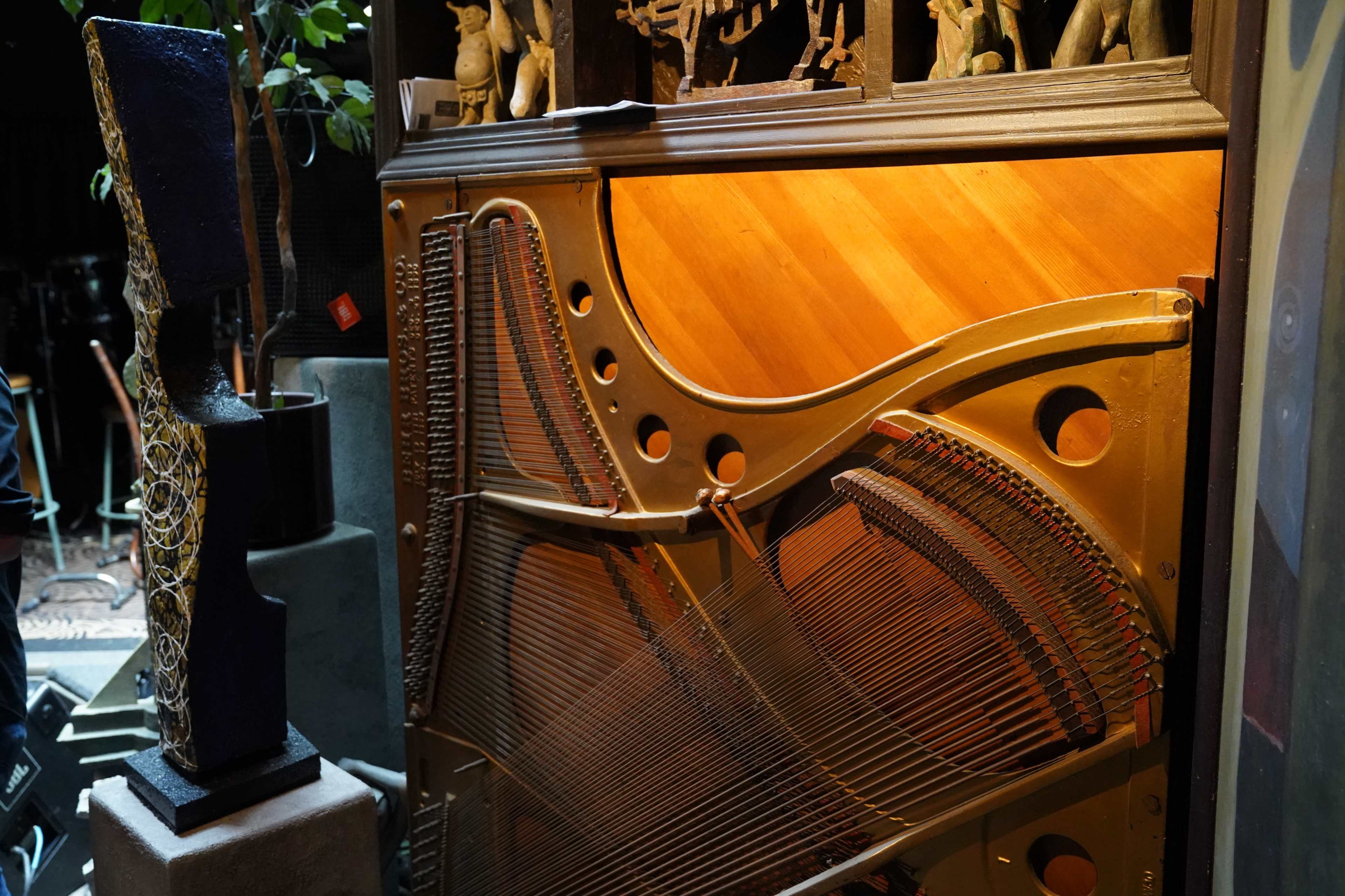The intricate inner mechanics of a grand piano alongside a sculptural piece in a dimly lit space.