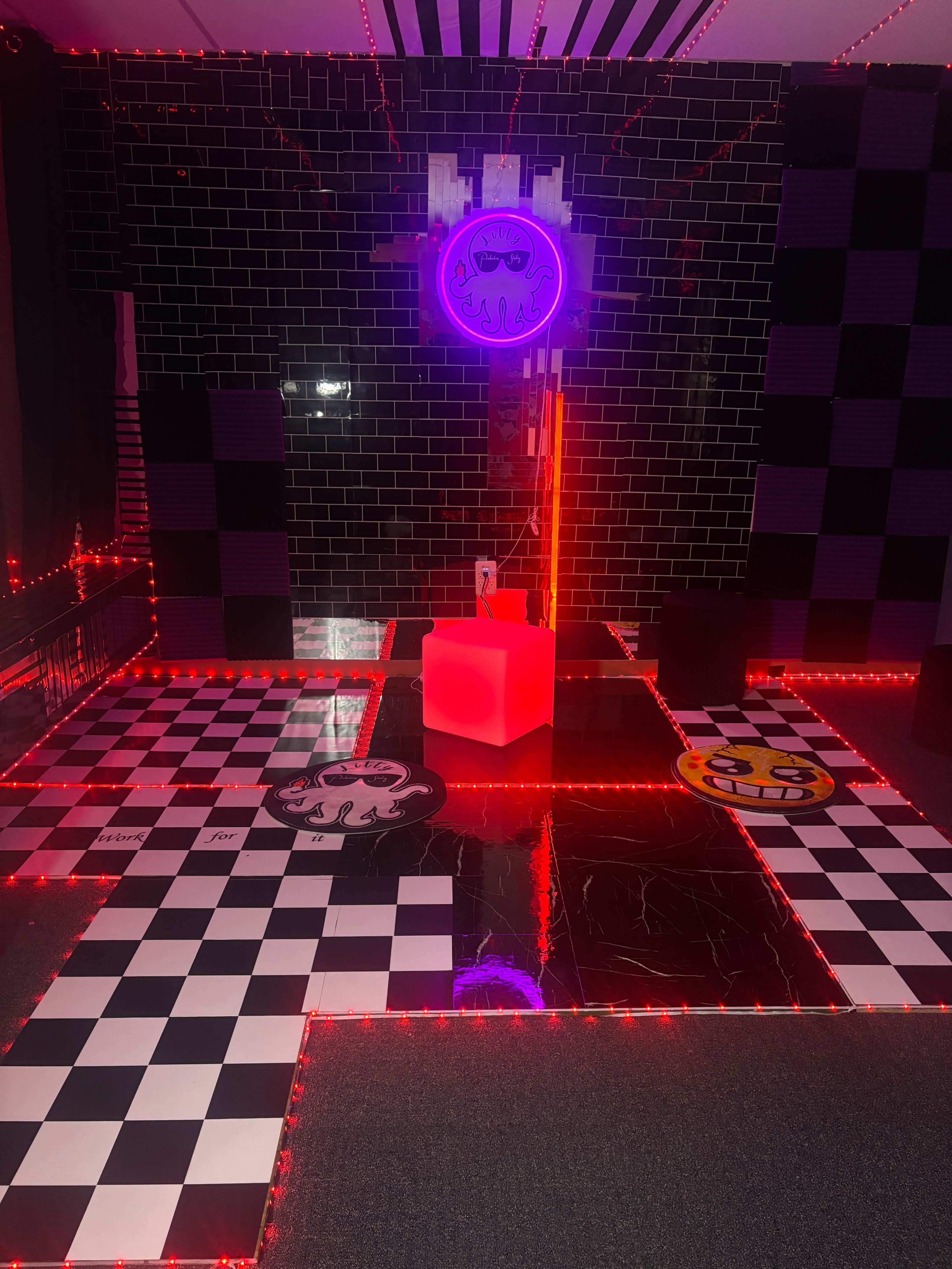 The image shows a room with black and white checkerboard flooring, a bright red block in the center, and neon lighting creating a vibrant atmosphere.