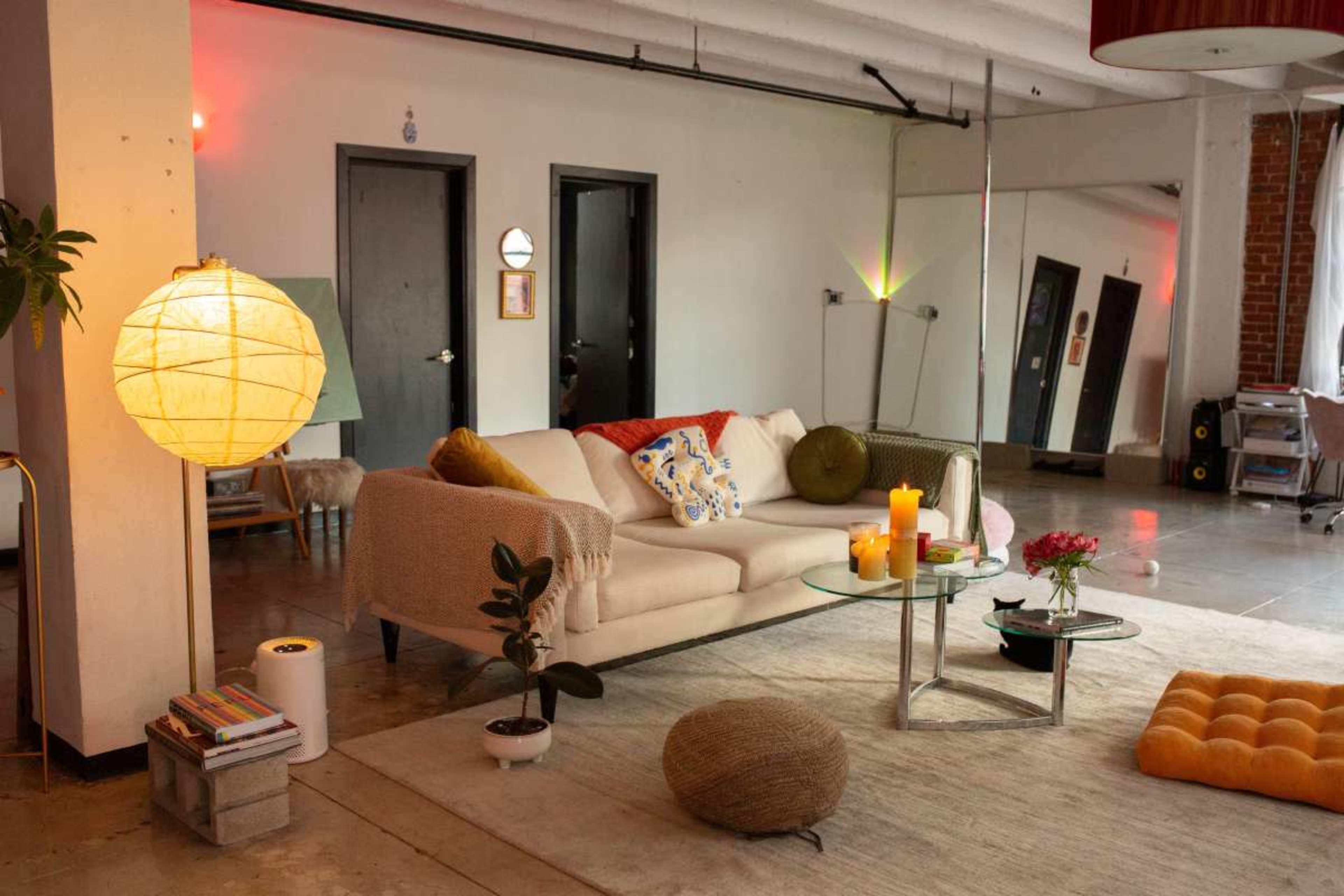 The image shows a modern living room with a white sofa, a glass coffee table, and decorative elements including candles, a plant, and a colorful throw.