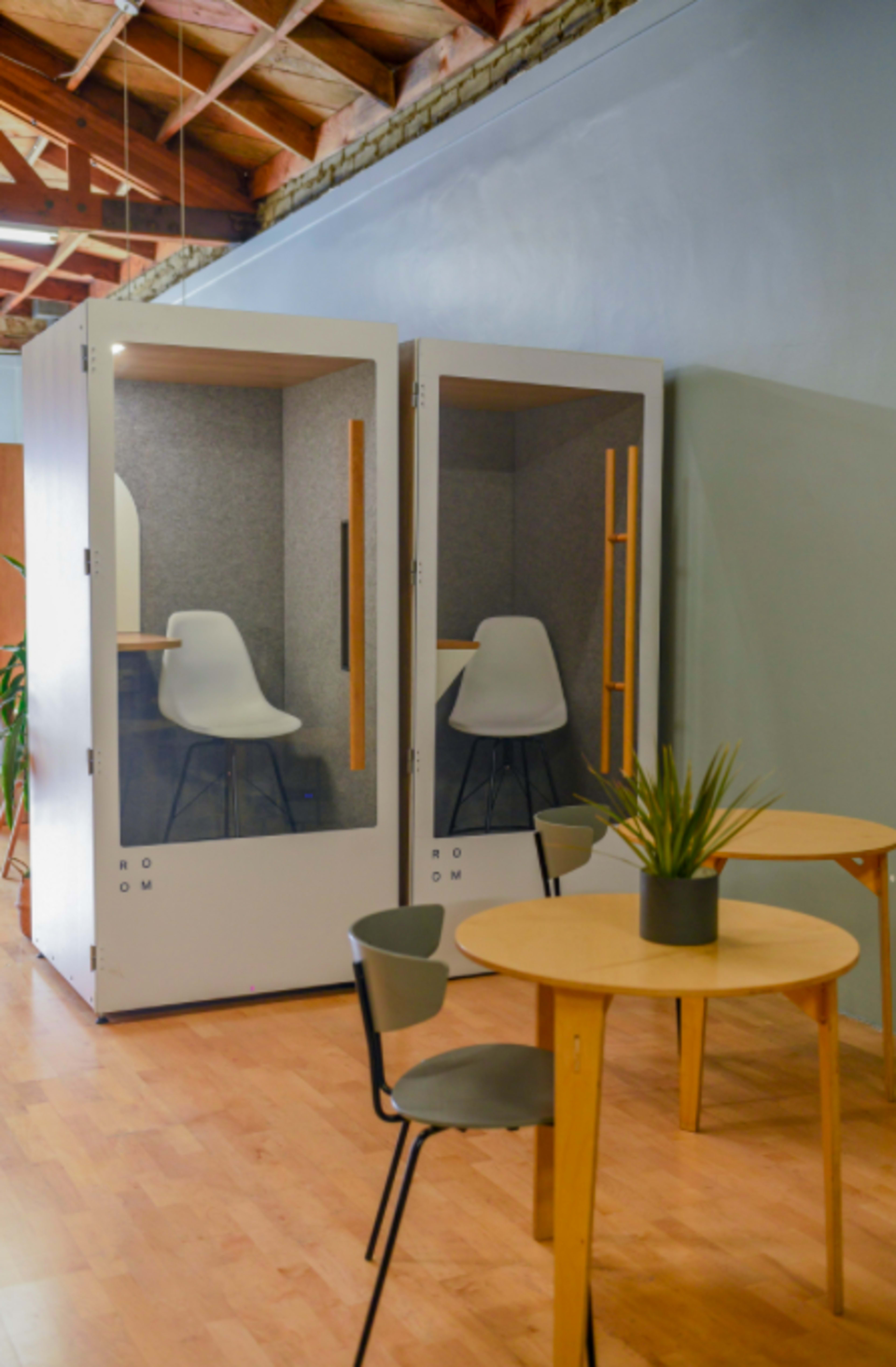 Two glass-walled study pods beside two small round tables with chairs in a modern workspace.