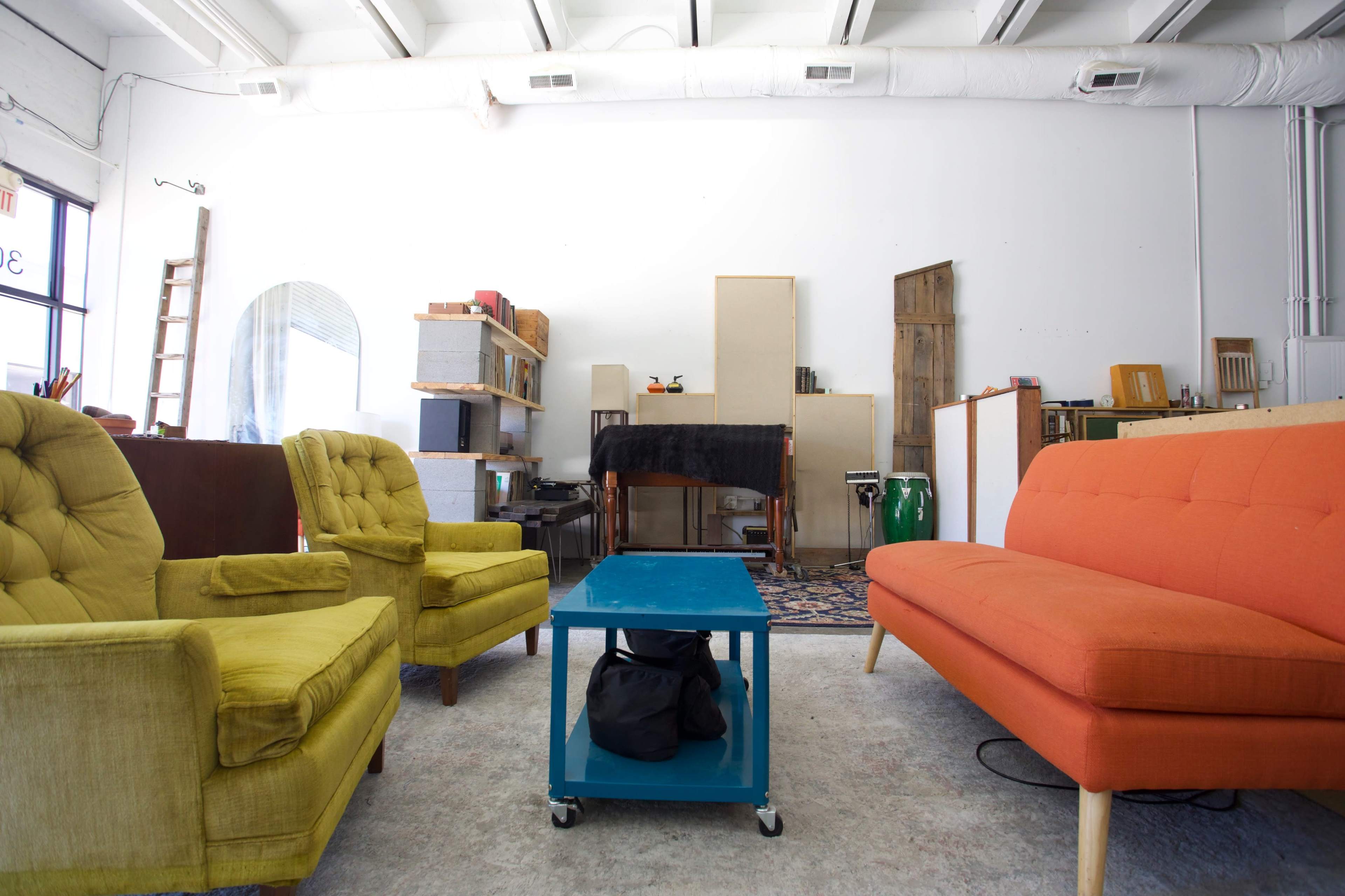A spacious room with colorful seating, including a yellow armchair and an orange couch, alongside a blue coffee table and various storage furniture against the walls.