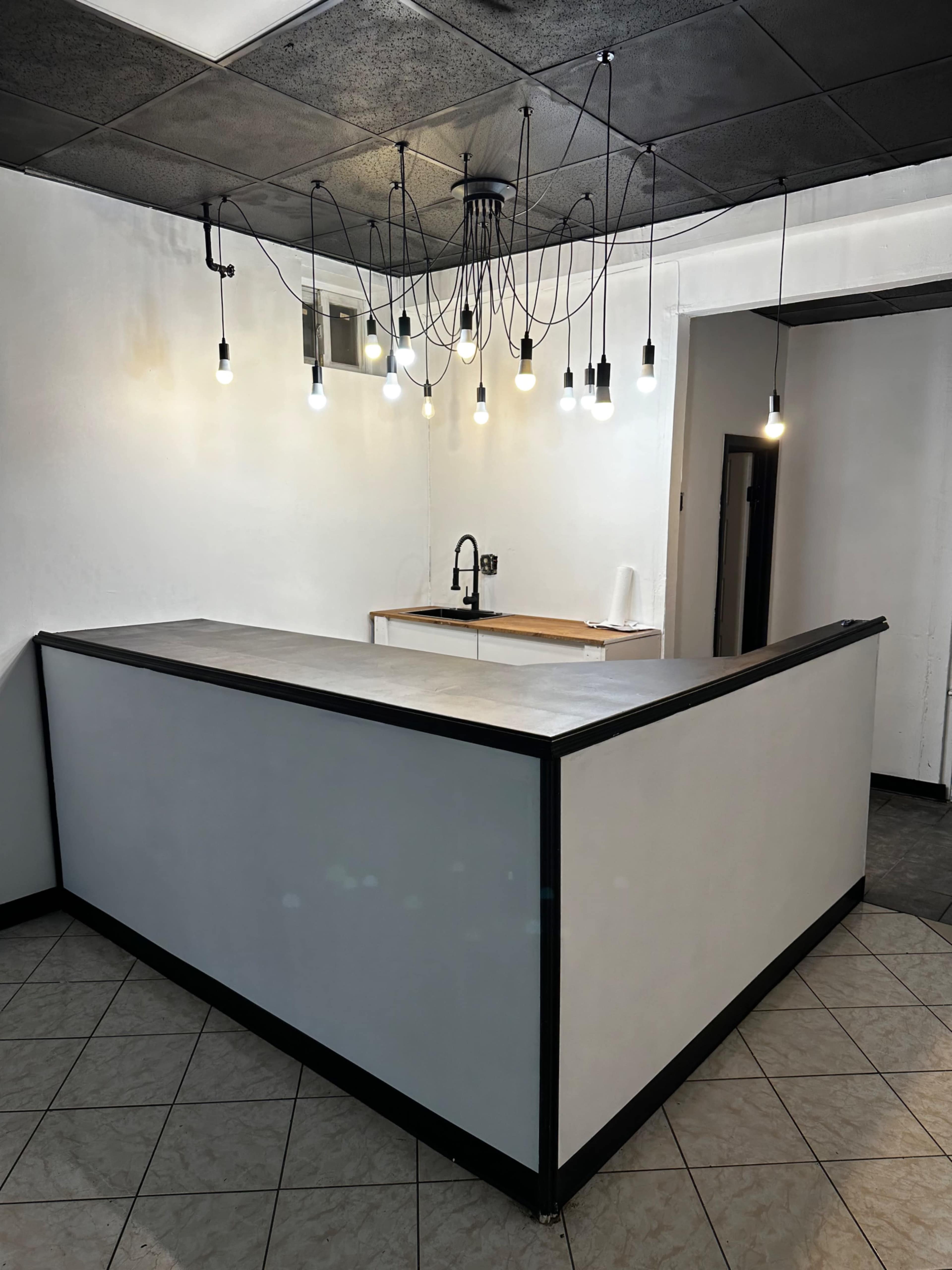 The image shows a minimalist reception area with a white counter and a hanging light fixture featuring multiple bulbs.