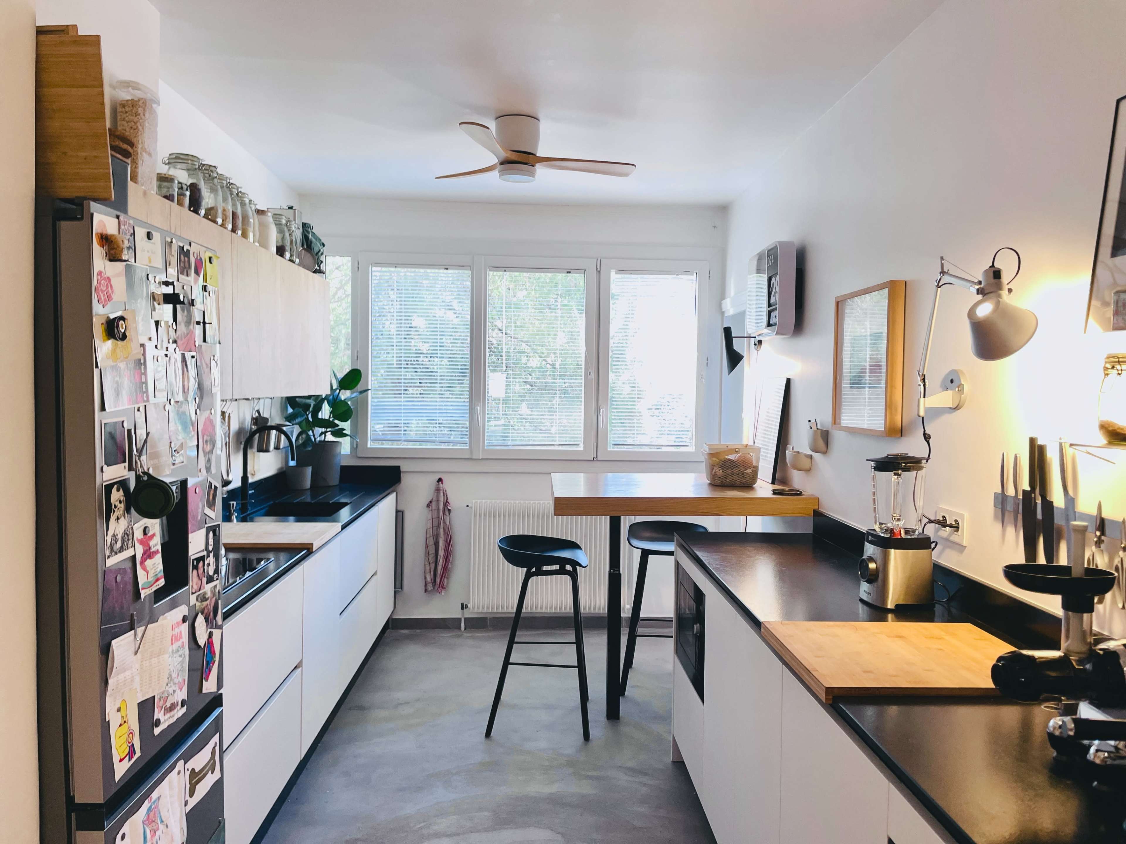 The kitchen features black countertops, white cabinetry, a dining table, and large windows that allow natural light to enter.