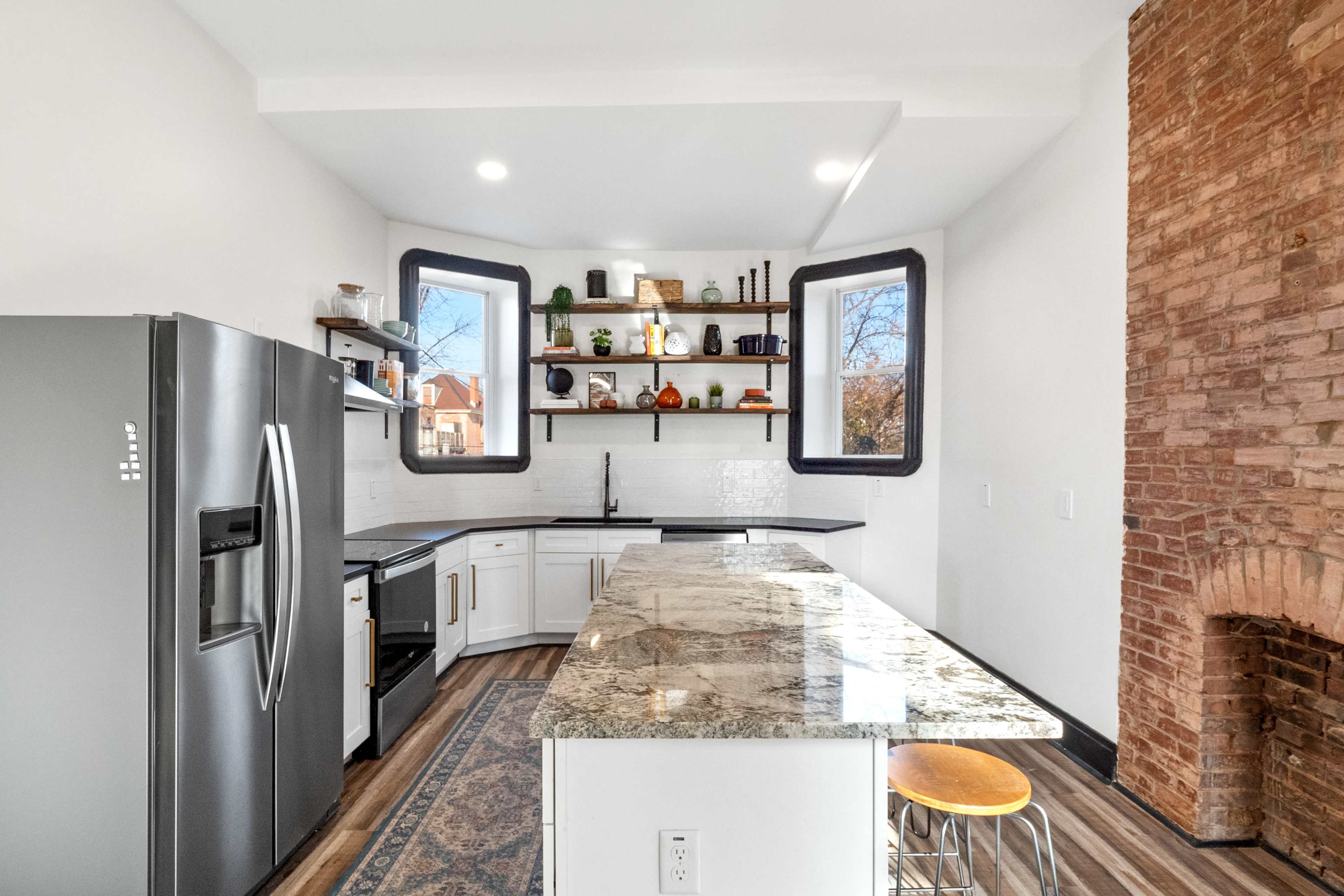A modern kitchen features stainless steel appliances, white cabinets, and a large granite countertop with shelves displaying various kitchen items.