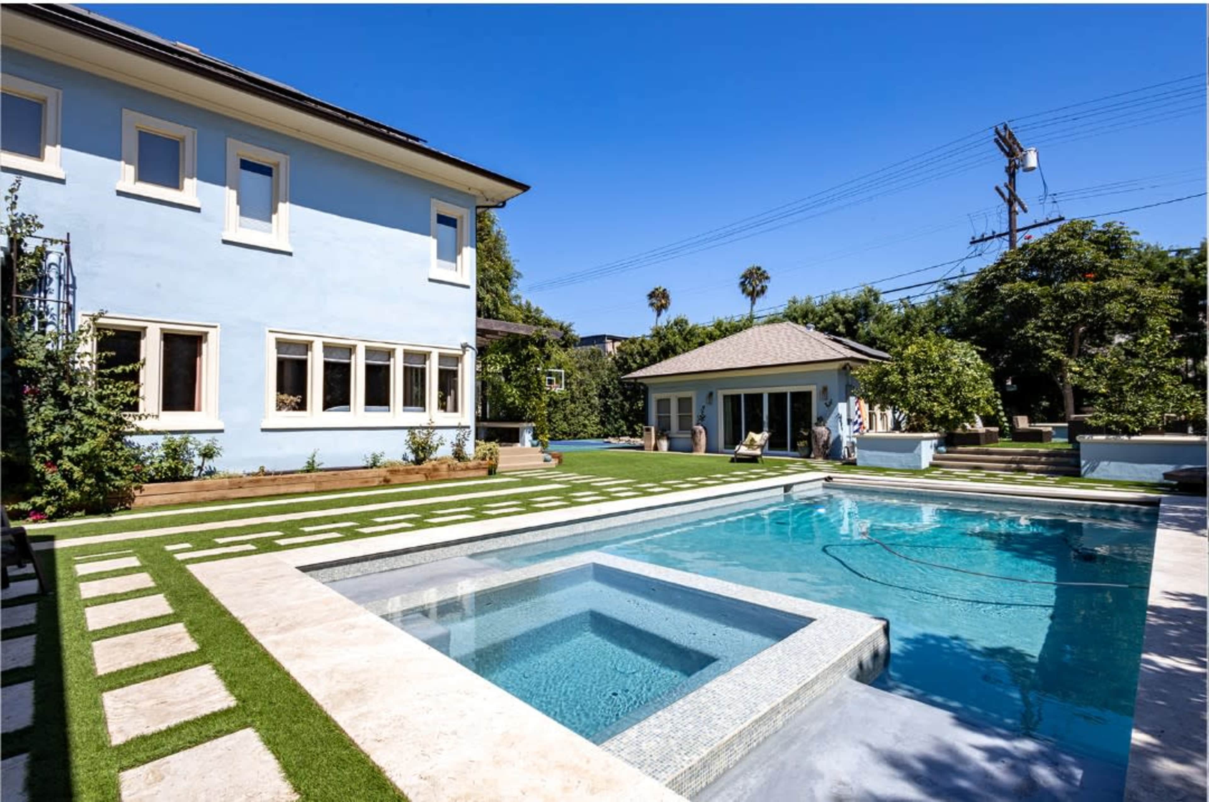 The image shows a blue house with a swimming pool and spa in a landscaped backyard surrounded by greenery.