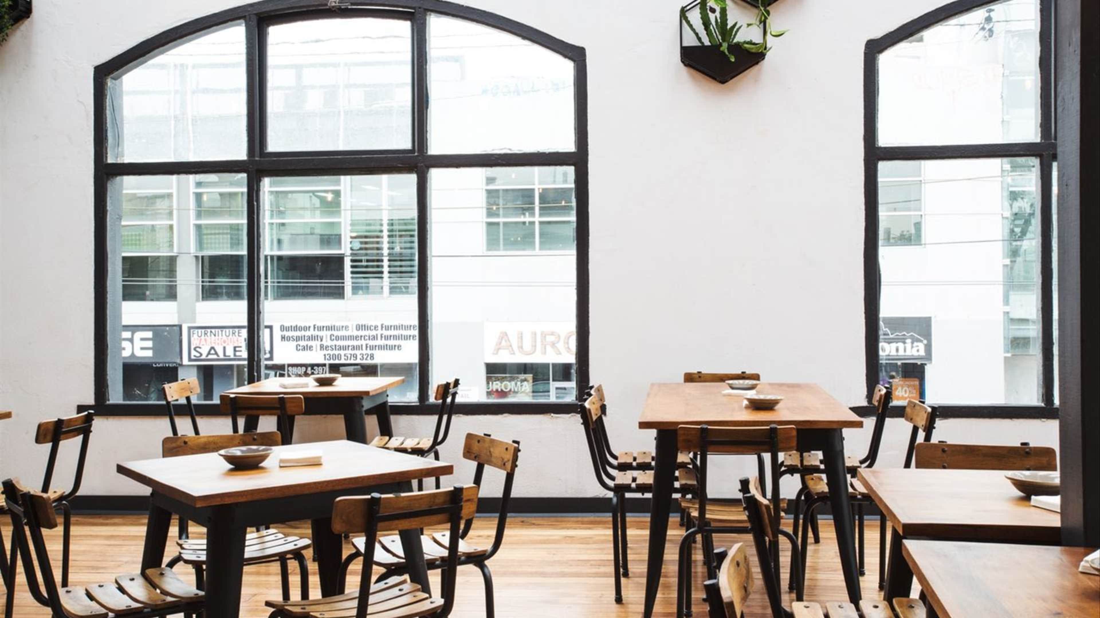 The image shows a spacious café interior with wooden tables and chairs arranged near large windows.