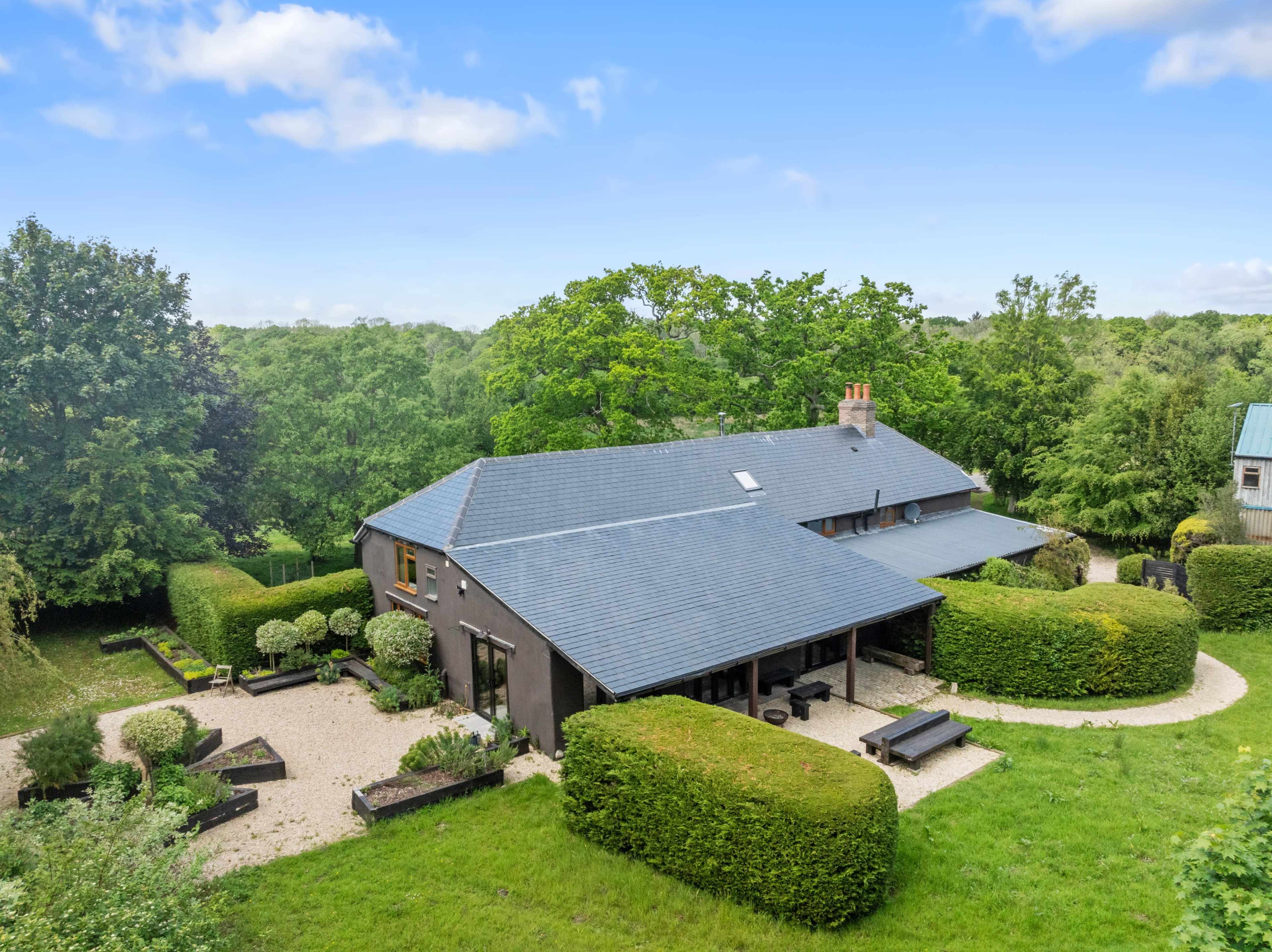 A spacious house with a gray roof is surrounded by well-maintained greenery and garden pathways.