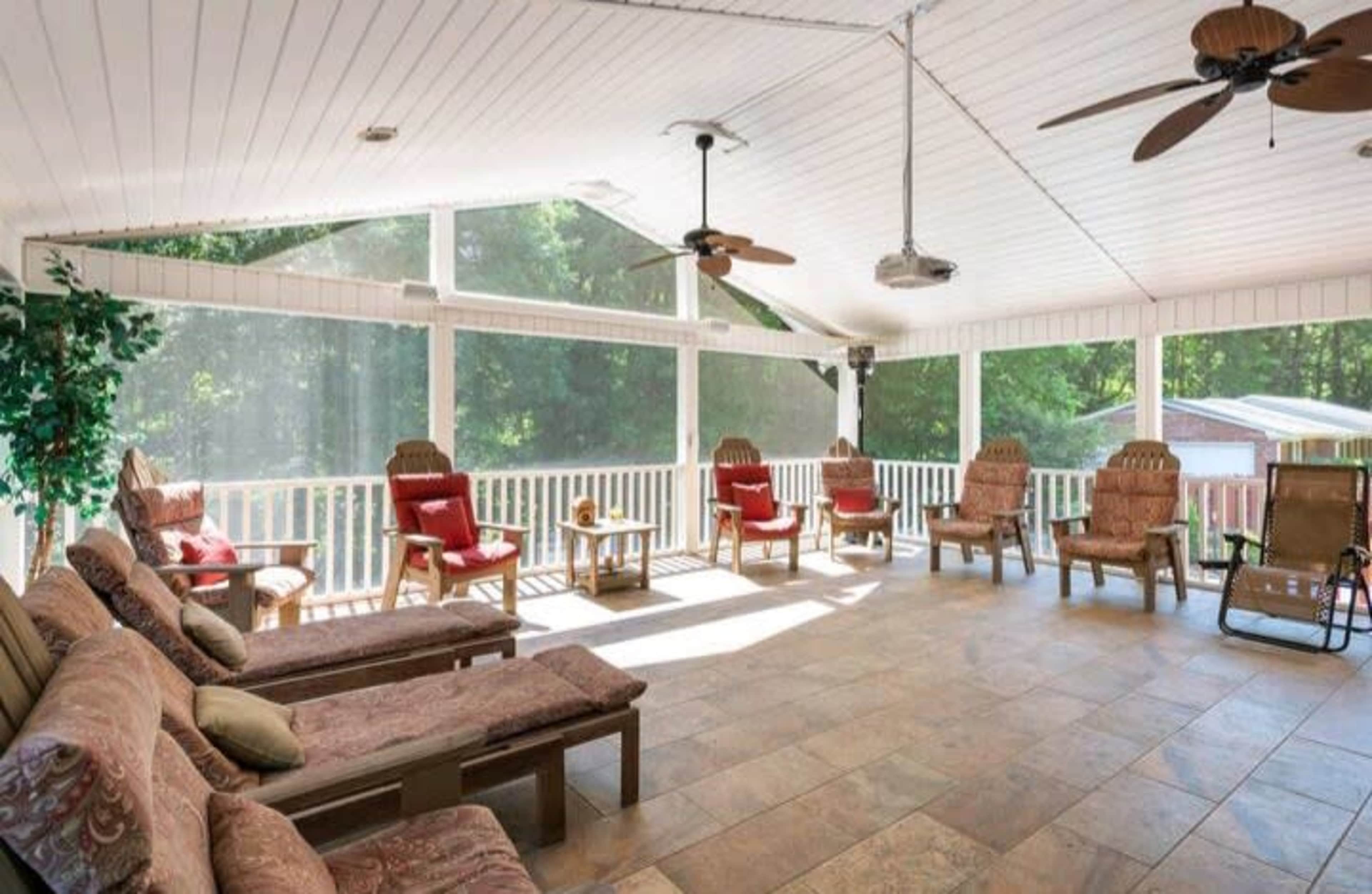 A spacious sunroom with tiled flooring, comfortable seating, and large windows overlooking a wooded area.