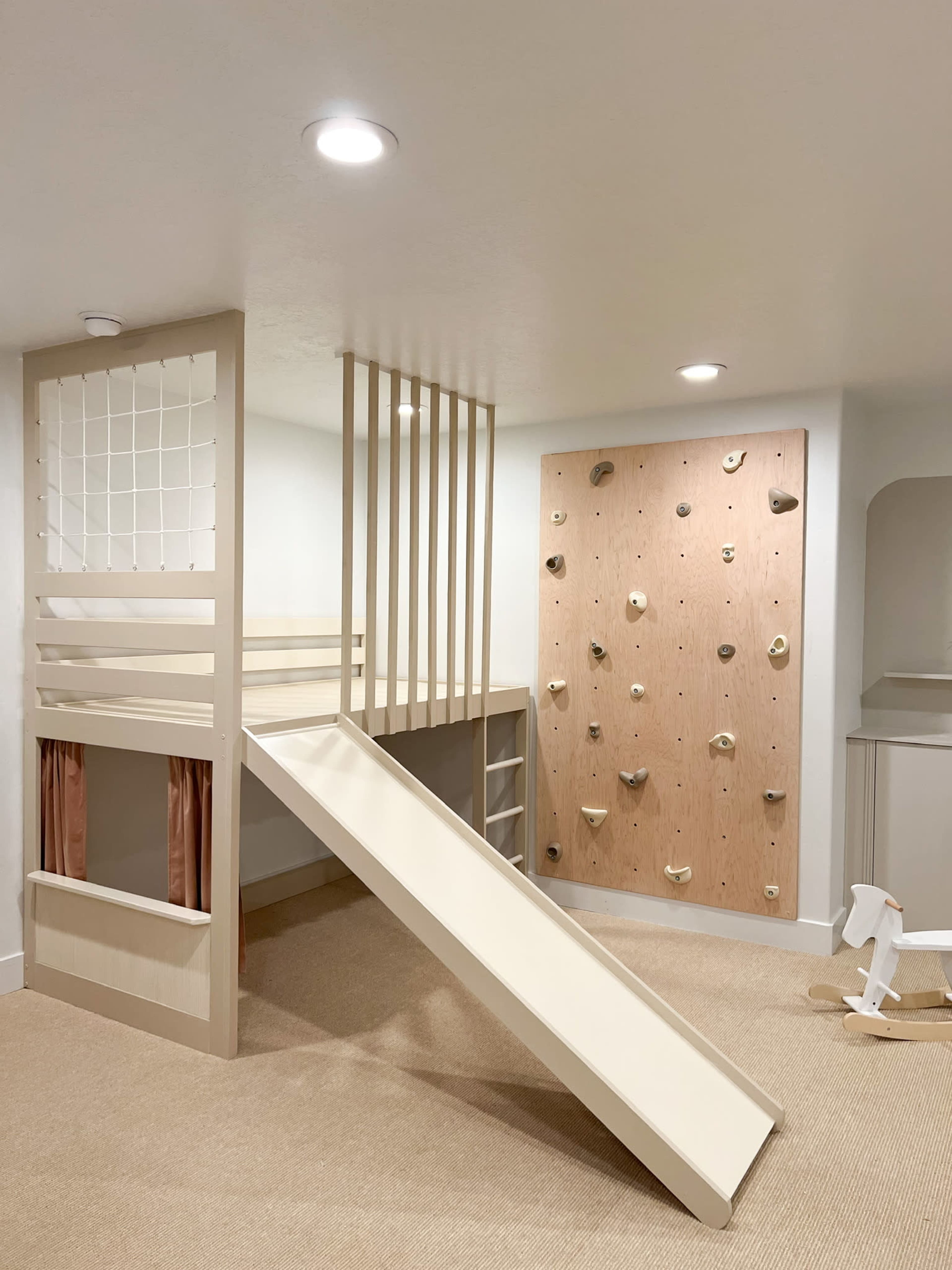 A children's playroom with a lofted bed featuring a slide and a climbing wall adjacent to it.