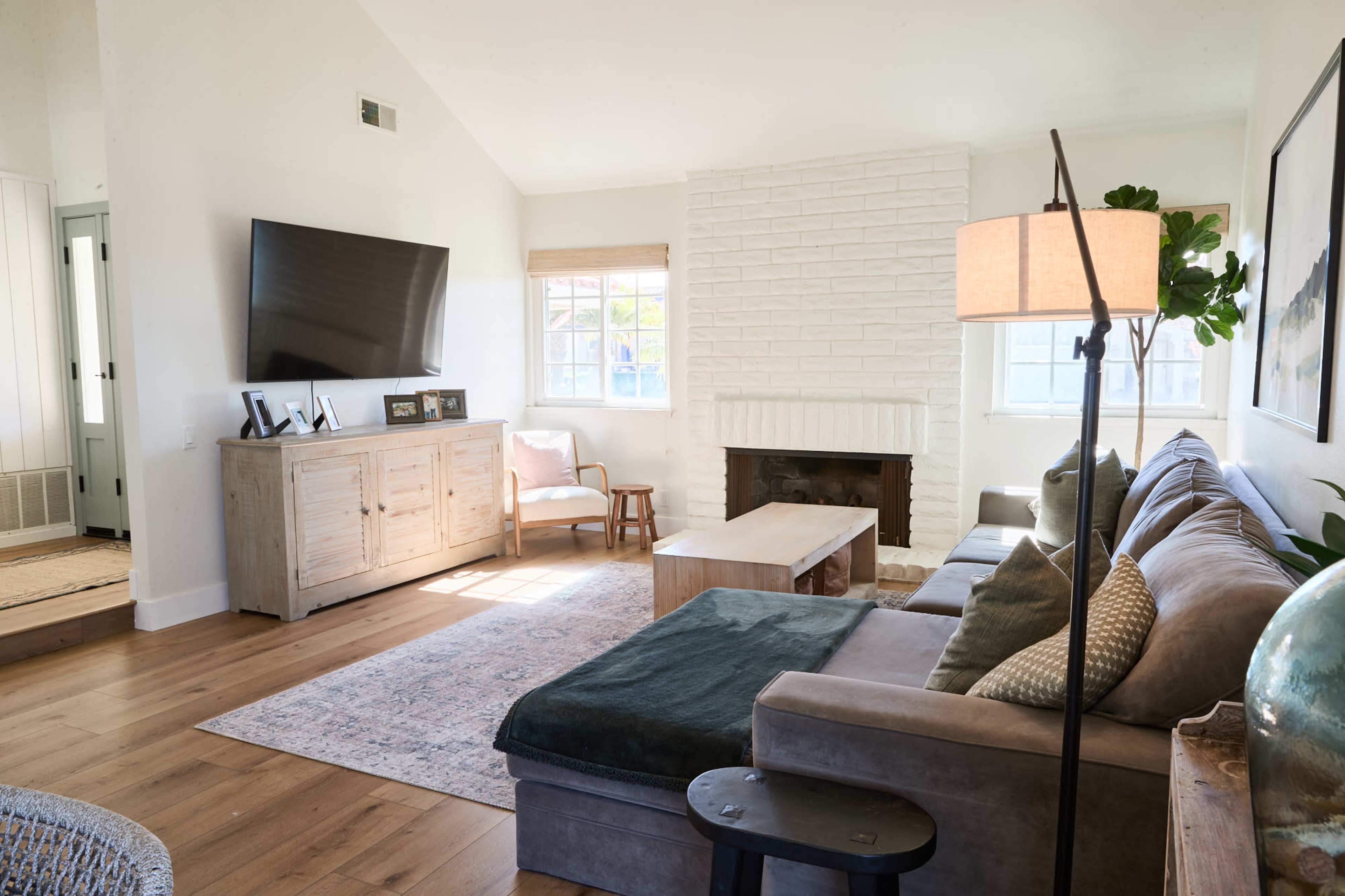 A bright living room featuring a sectional sofa, a wooden coffee table, a television mounted on the wall, and a light-colored rug.