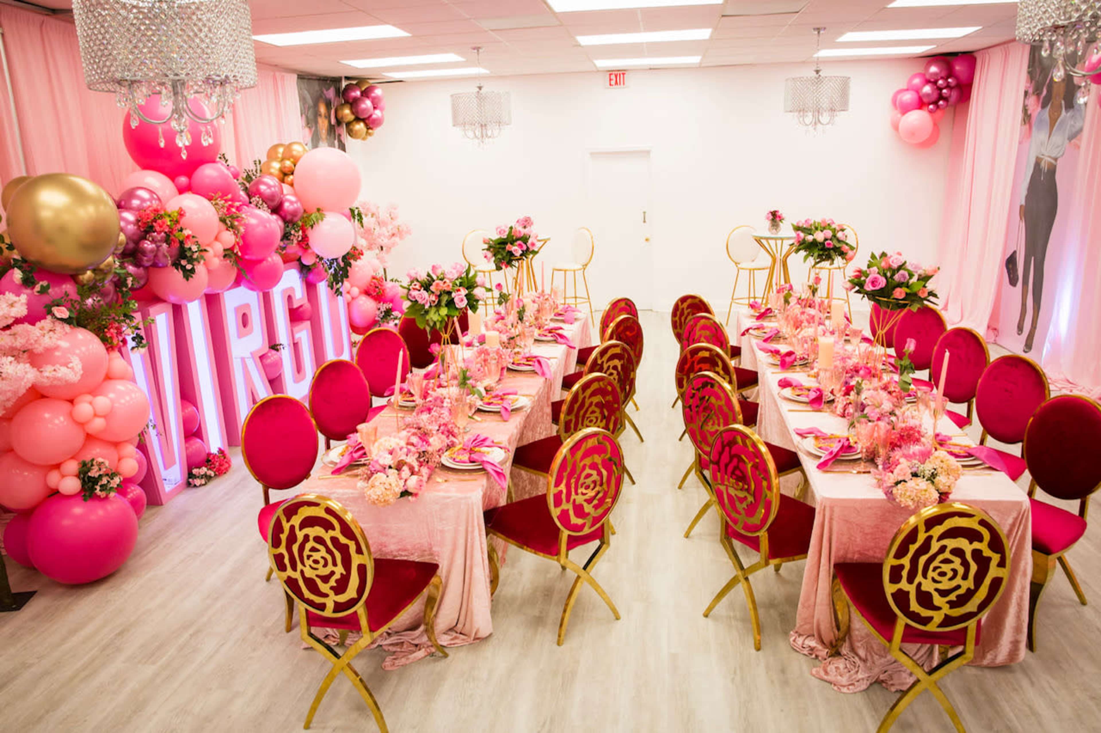 A lavish party setting with pink-themed decorations, including tables adorned with floral arrangements and a backdrop featuring the word "VIRGO" in large letters, surrounded by balloons.
