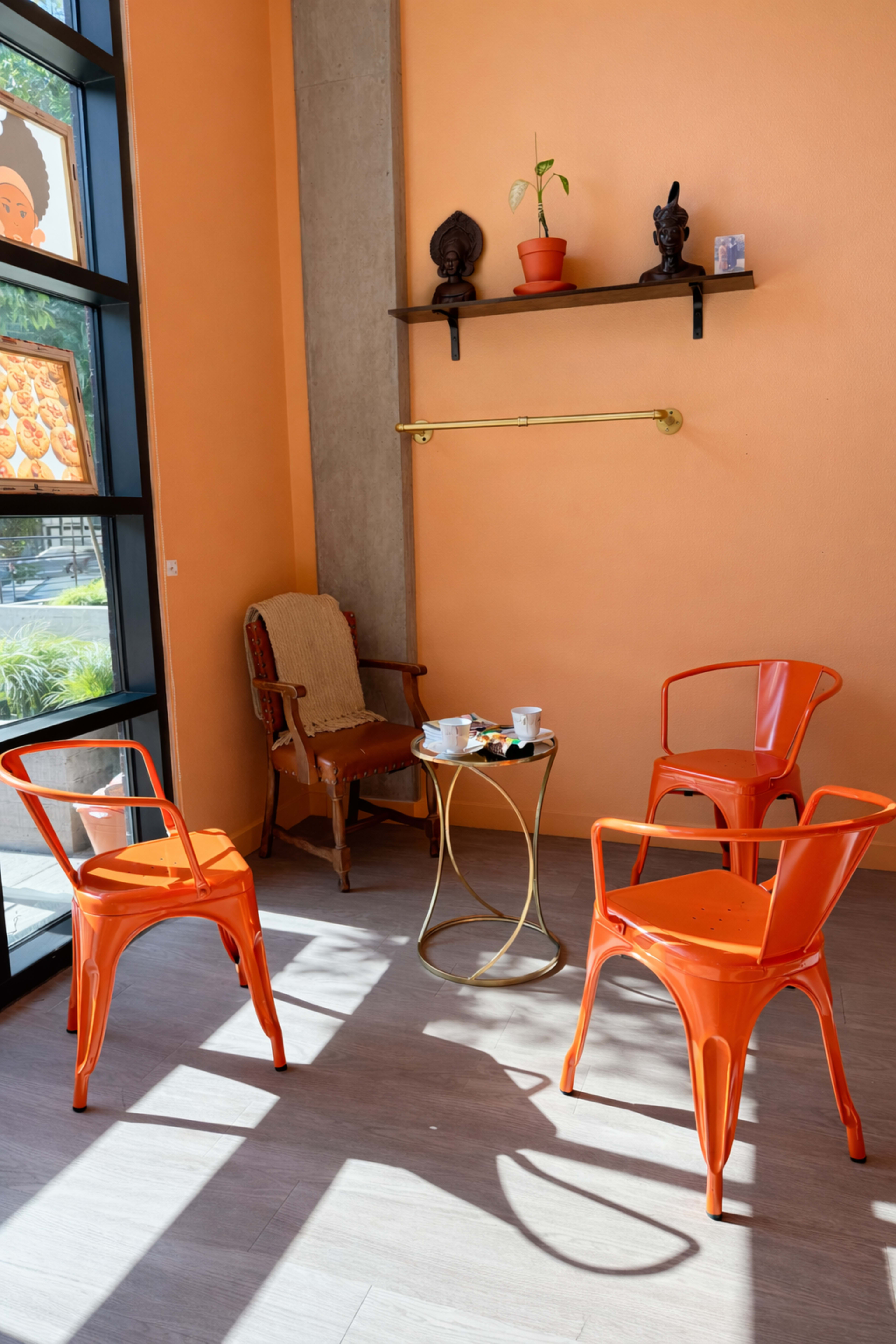 The image shows a cozy seating area with four orange chairs surrounding a small golden table against an orange wall, featuring a plant and decorative items on a shelf.