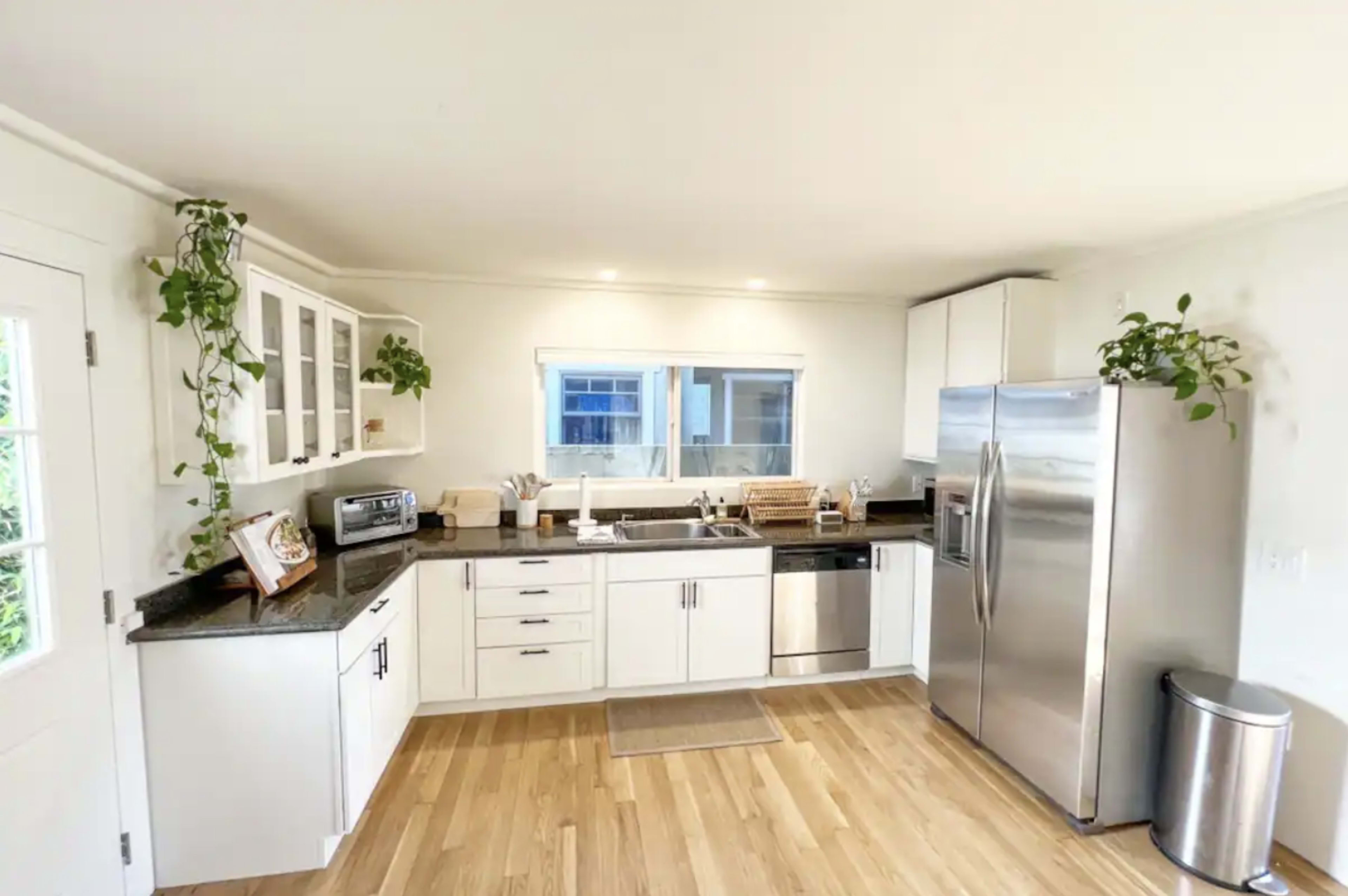 A modern kitchen with white cabinets, a stainless steel refrigerator, and a countertop with potted plants.
