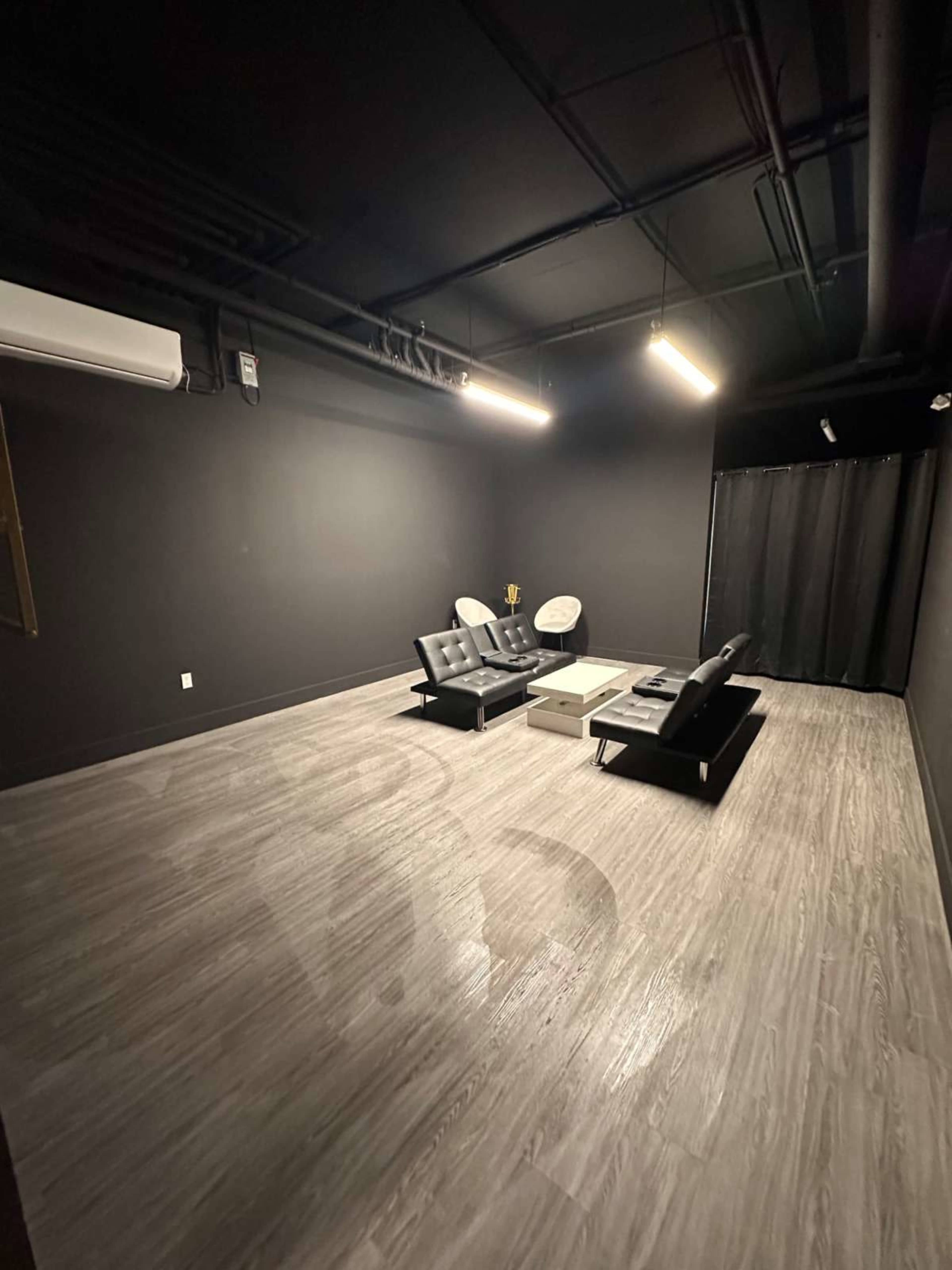 A minimalistic room with black walls, two black sofas, a coffee table, and a dark curtain in one corner.