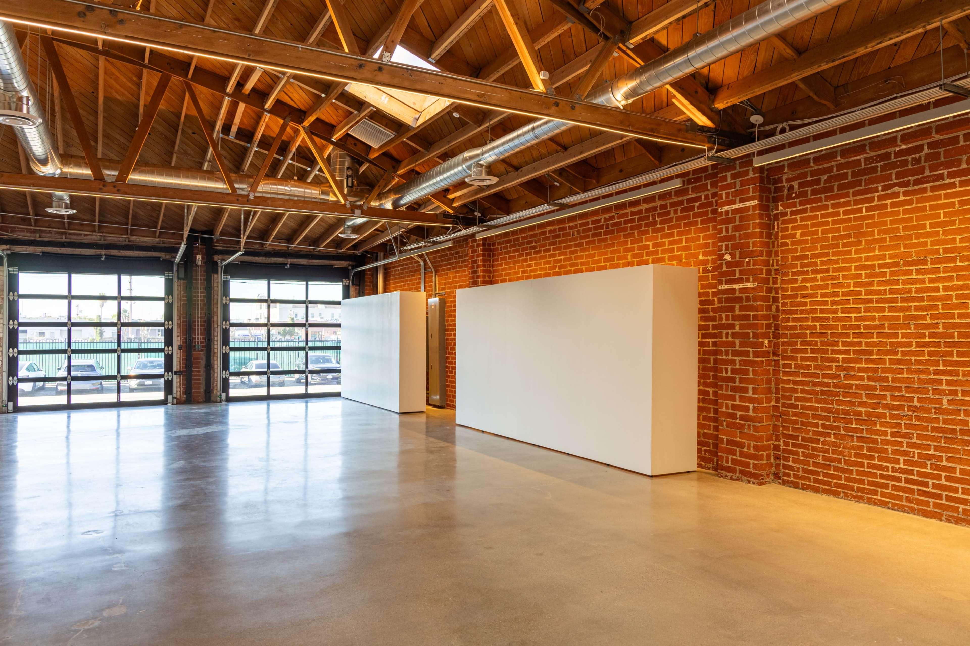 The image shows a spacious indoor area with exposed brick walls, wooden beams, and two white partition walls in a well-lit setting.