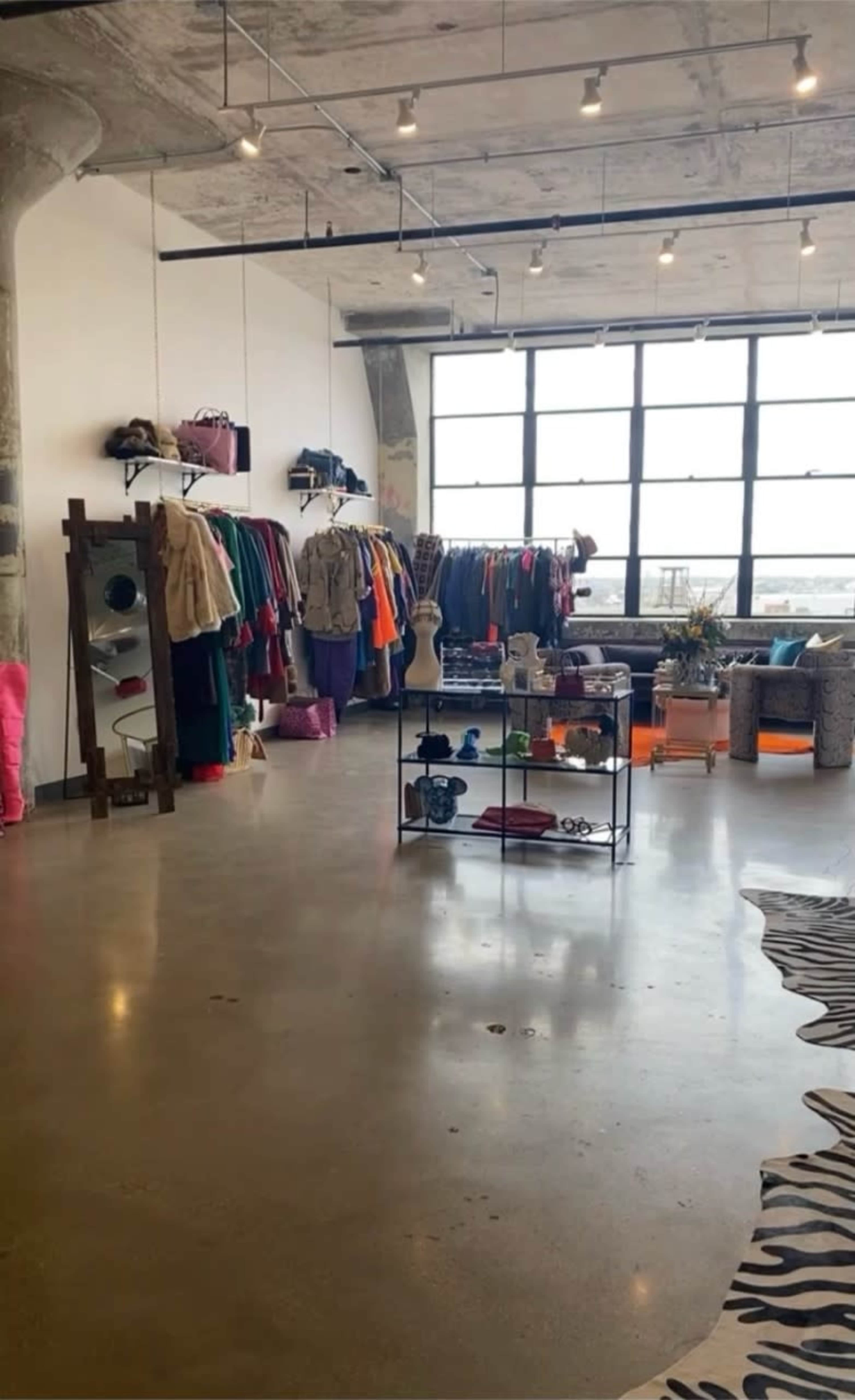 The image shows a boutique clothing store with racks of colorful apparel, a display table, and large windows allowing natural light to fill the space.