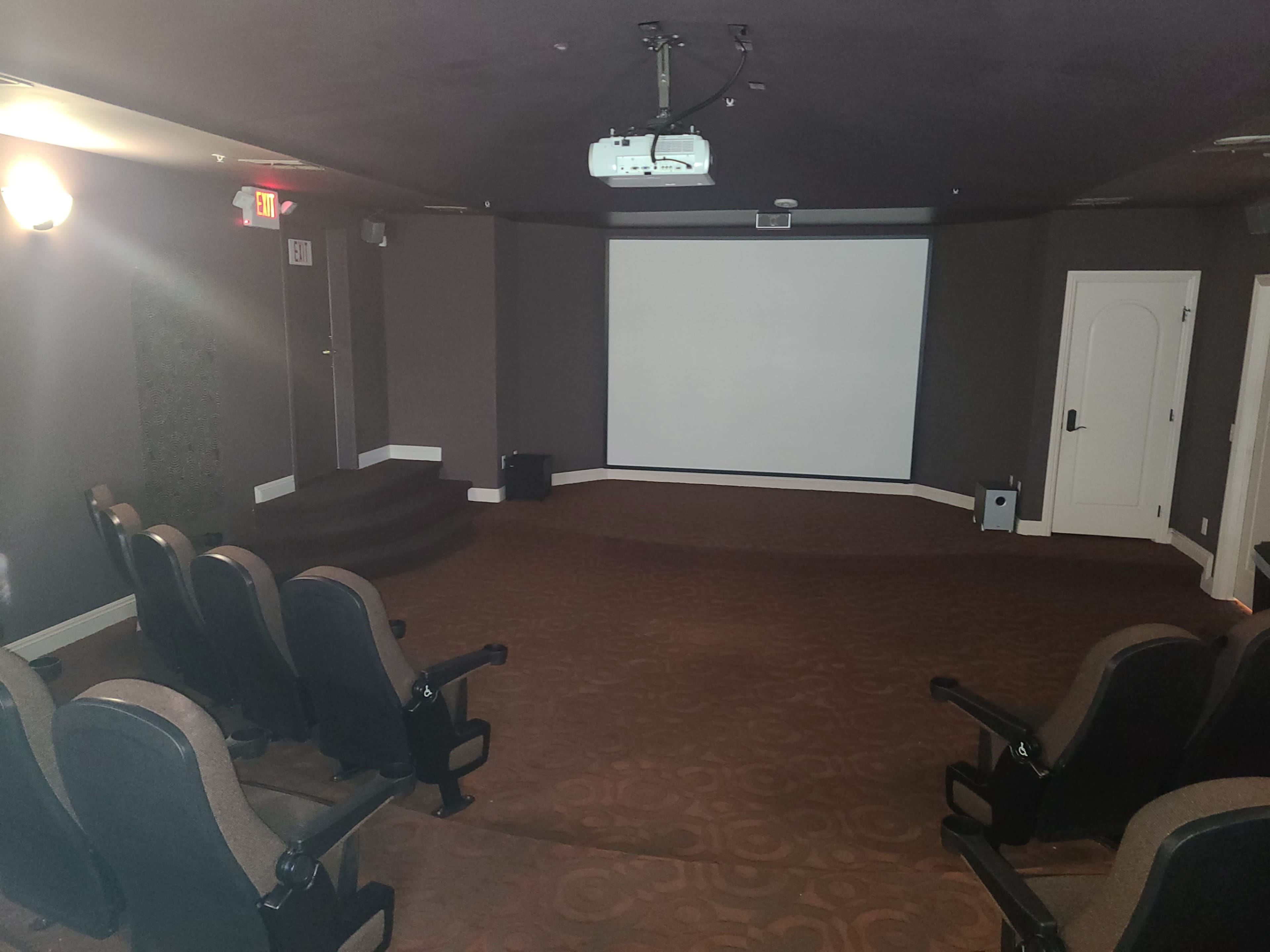 A private home theater featuring a blank screen at the front, tiered seating rows, and a projector mounted on the ceiling.