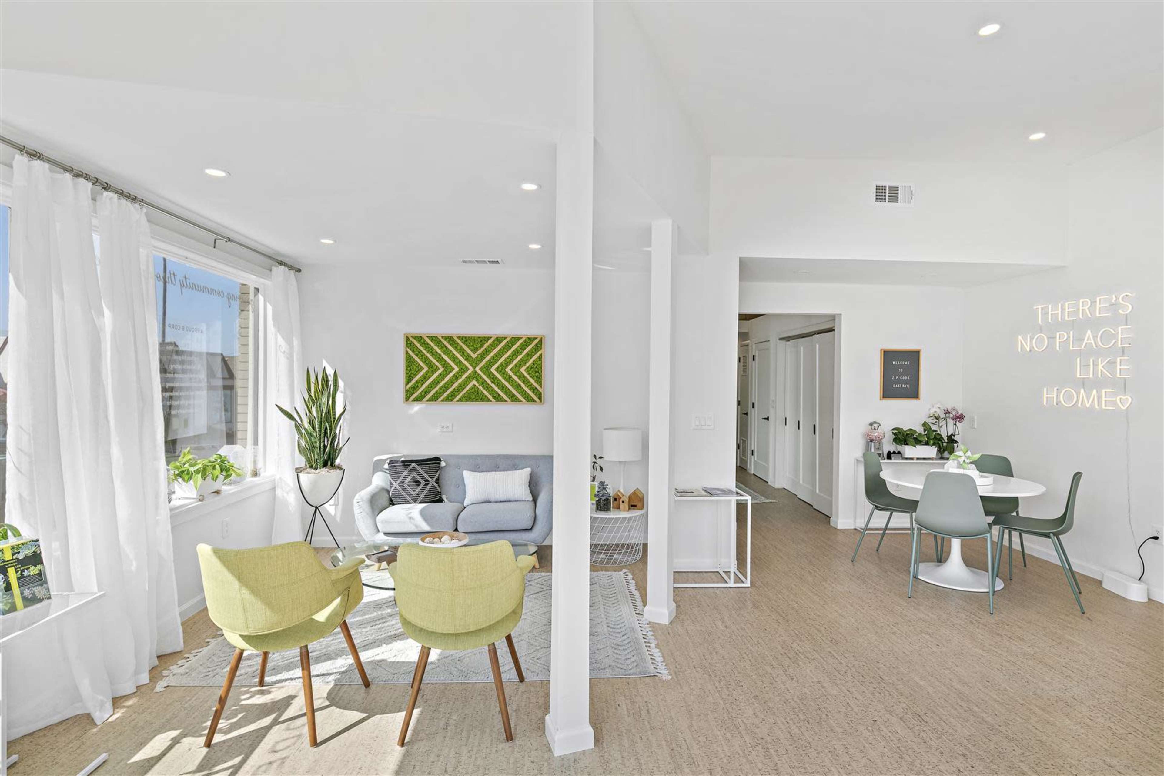 A bright, modern living space featuring a cozy seating area with a sofa and chairs, a dining area with a table and chairs, and large windows allowing natural light to enter.