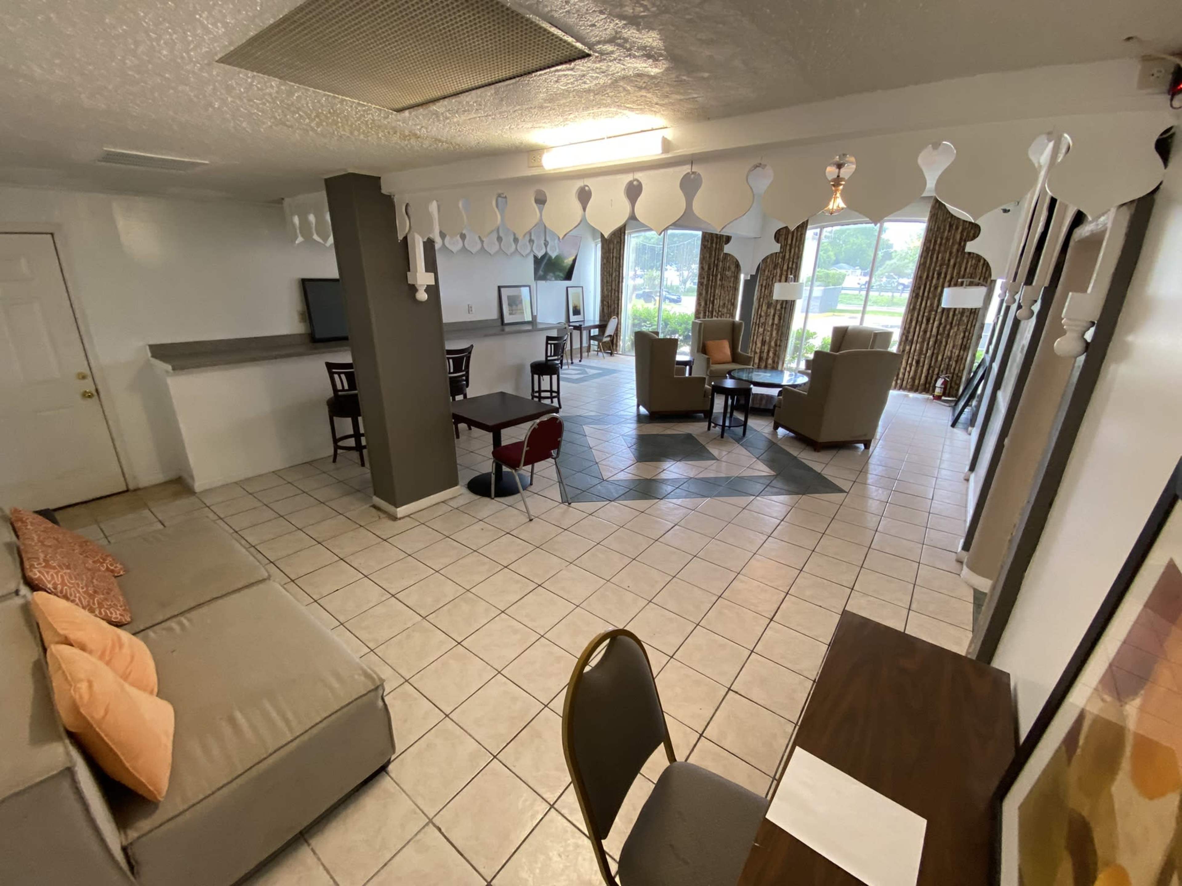 A spacious, open lounge area features a seating arrangement, dining tables, and large windows providing natural light.