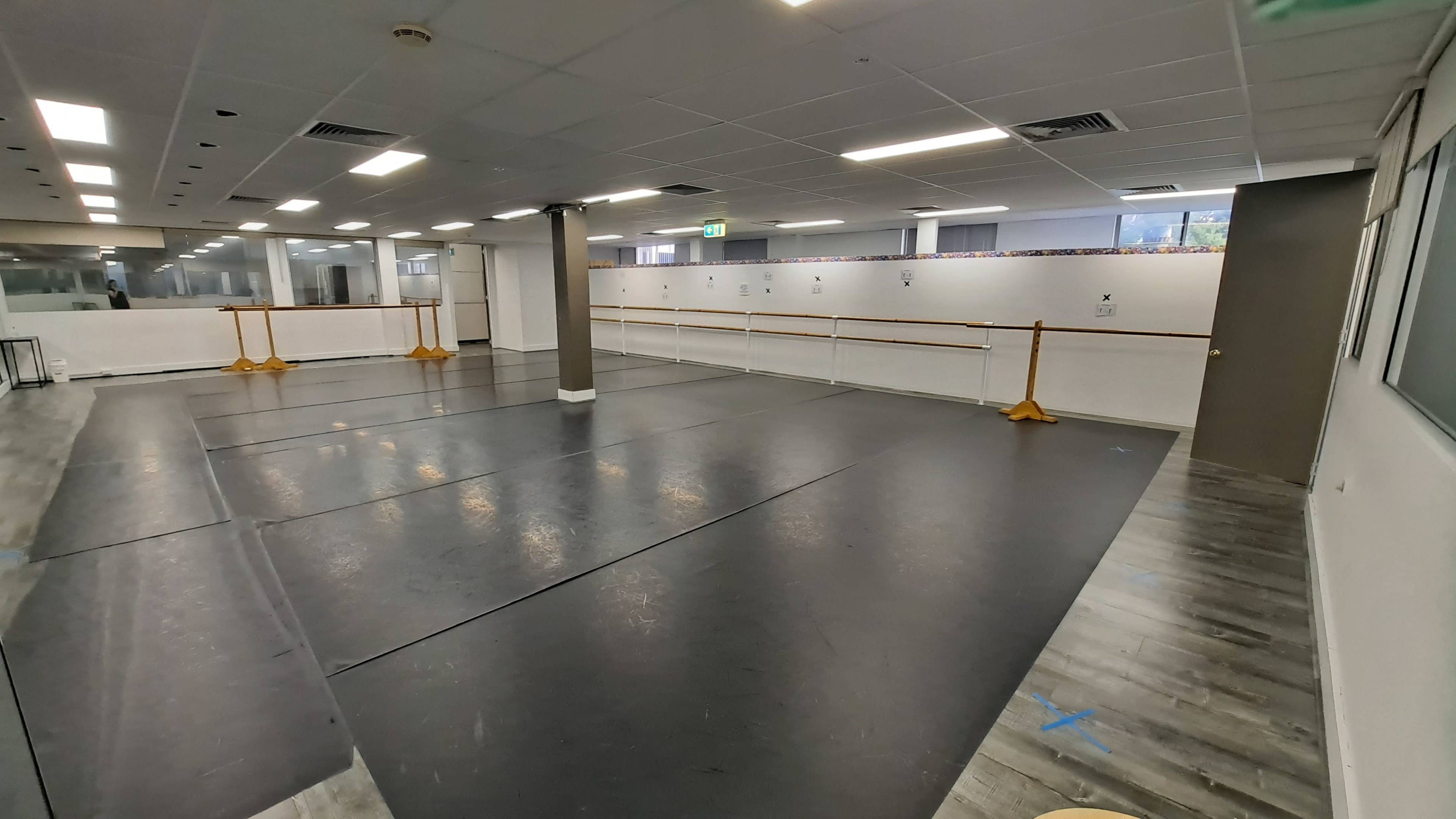 A spacious dance studio with a wooden floor, mirrored walls, and ballet barres along the sides.