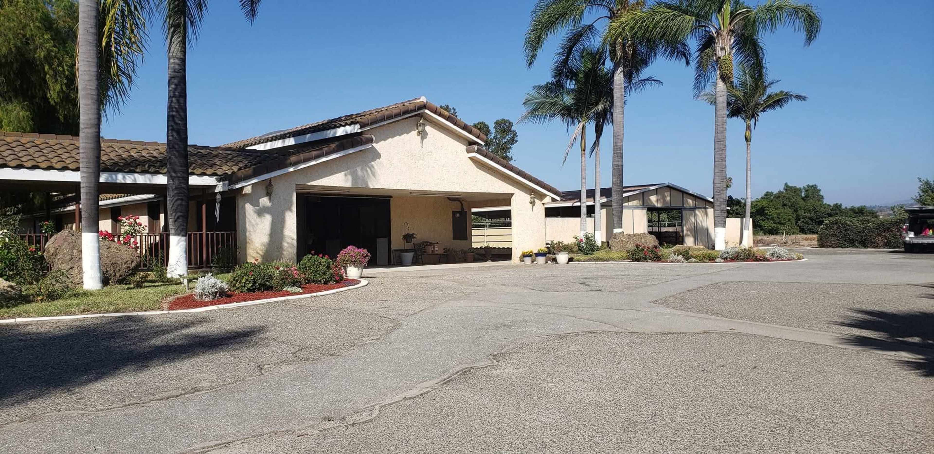 The image shows a residential property featuring a house with a tiled roof, palm trees, and a landscaped driveway.