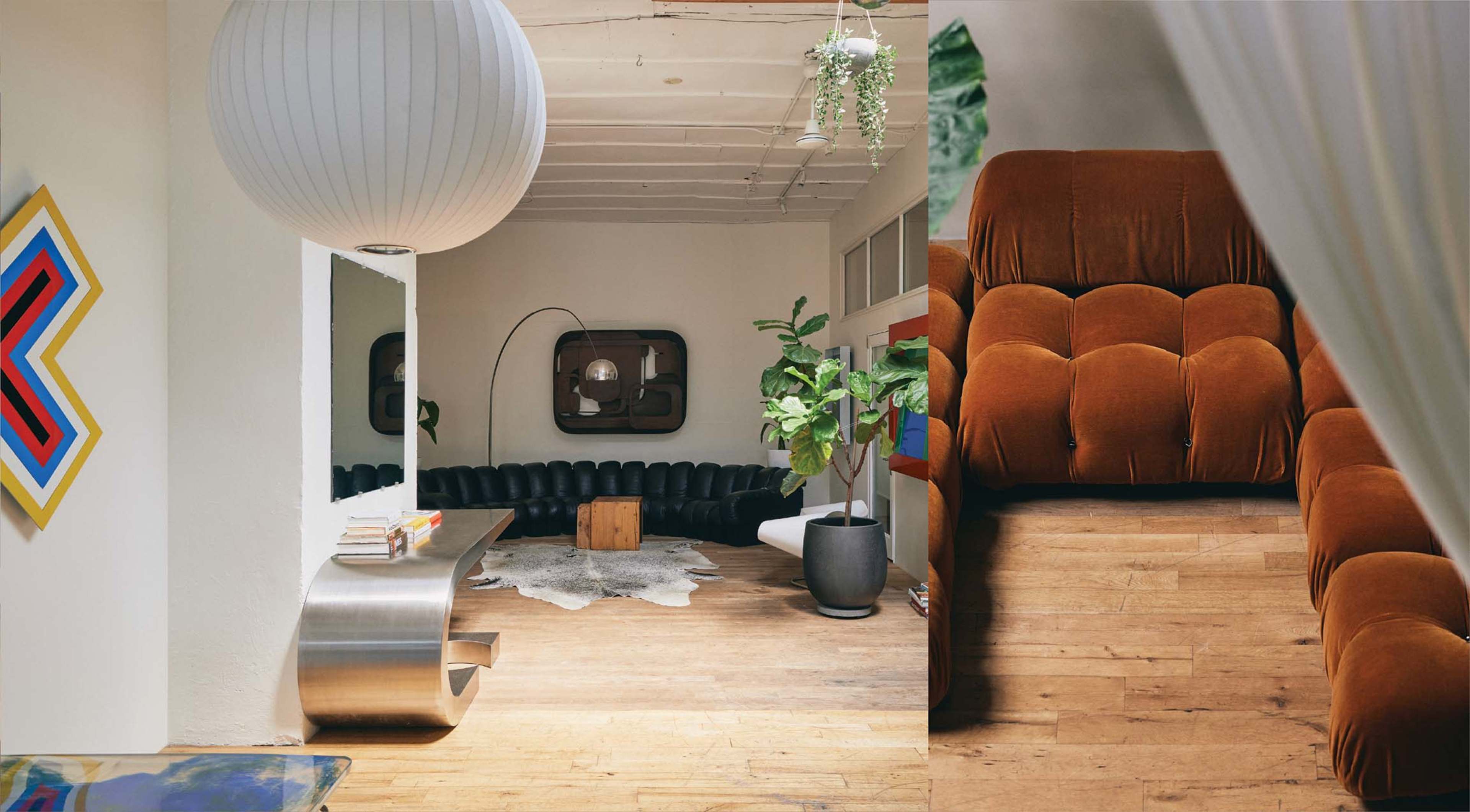 A spacious room with modern furniture, featuring a large black sectional sofa, a wooden floor, a round pendant light, and a potted plant.