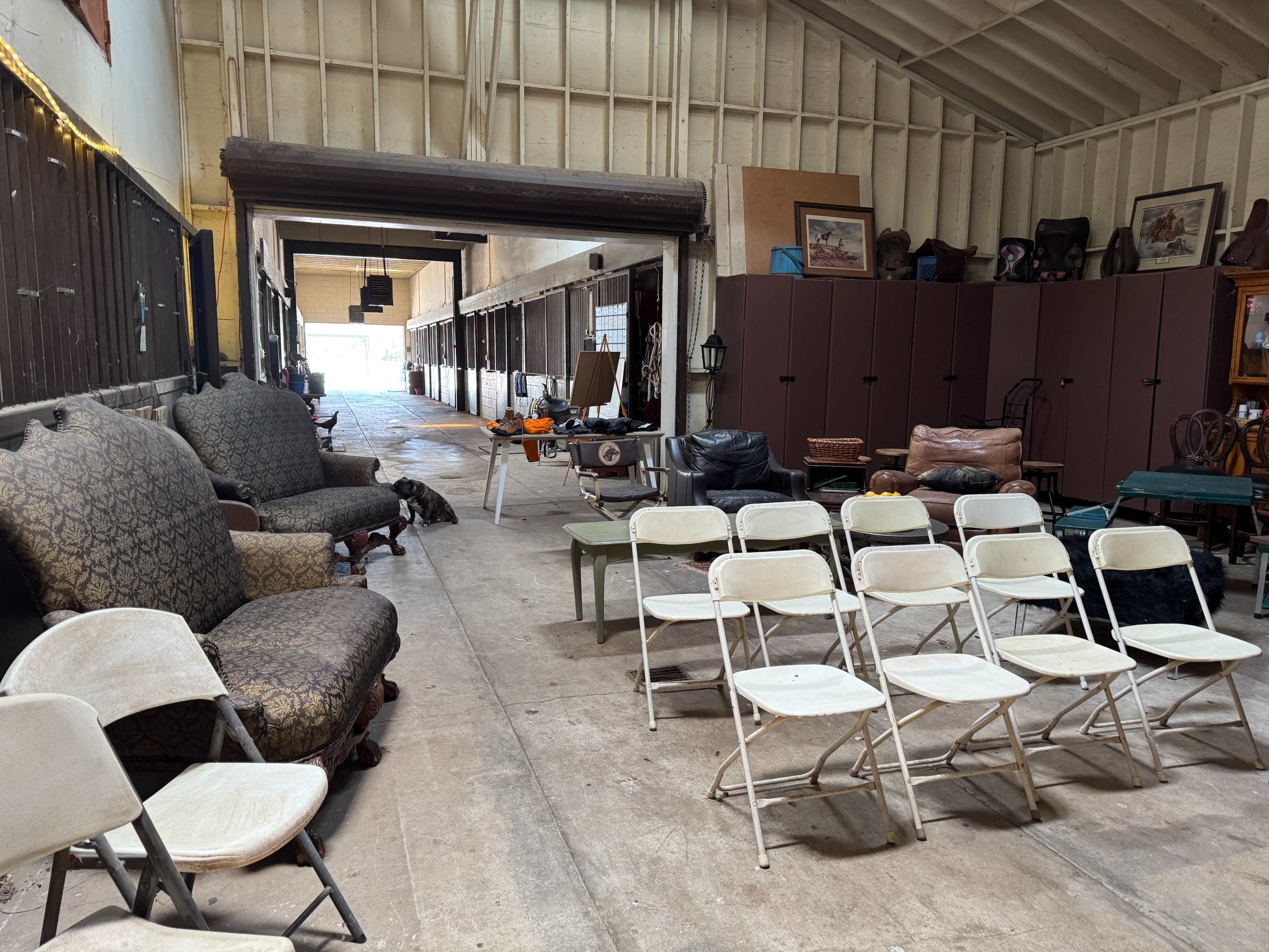 The image shows a long, narrow indoor space with several rows of chairs, a few pieces of furniture, and light streaming in from the far end.