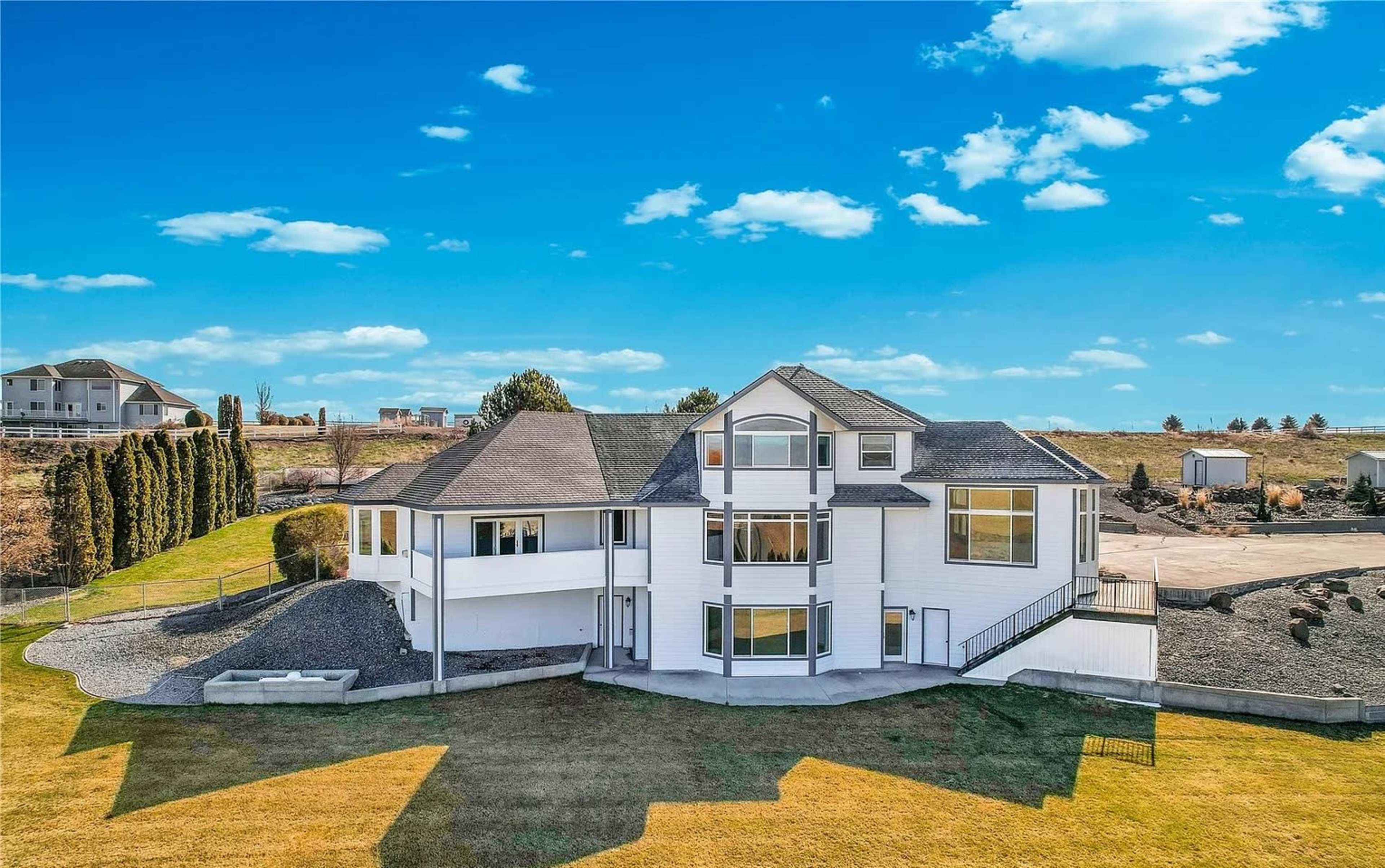 A modern two-story house with large windows and a landscaped yard is situated on a hillside.