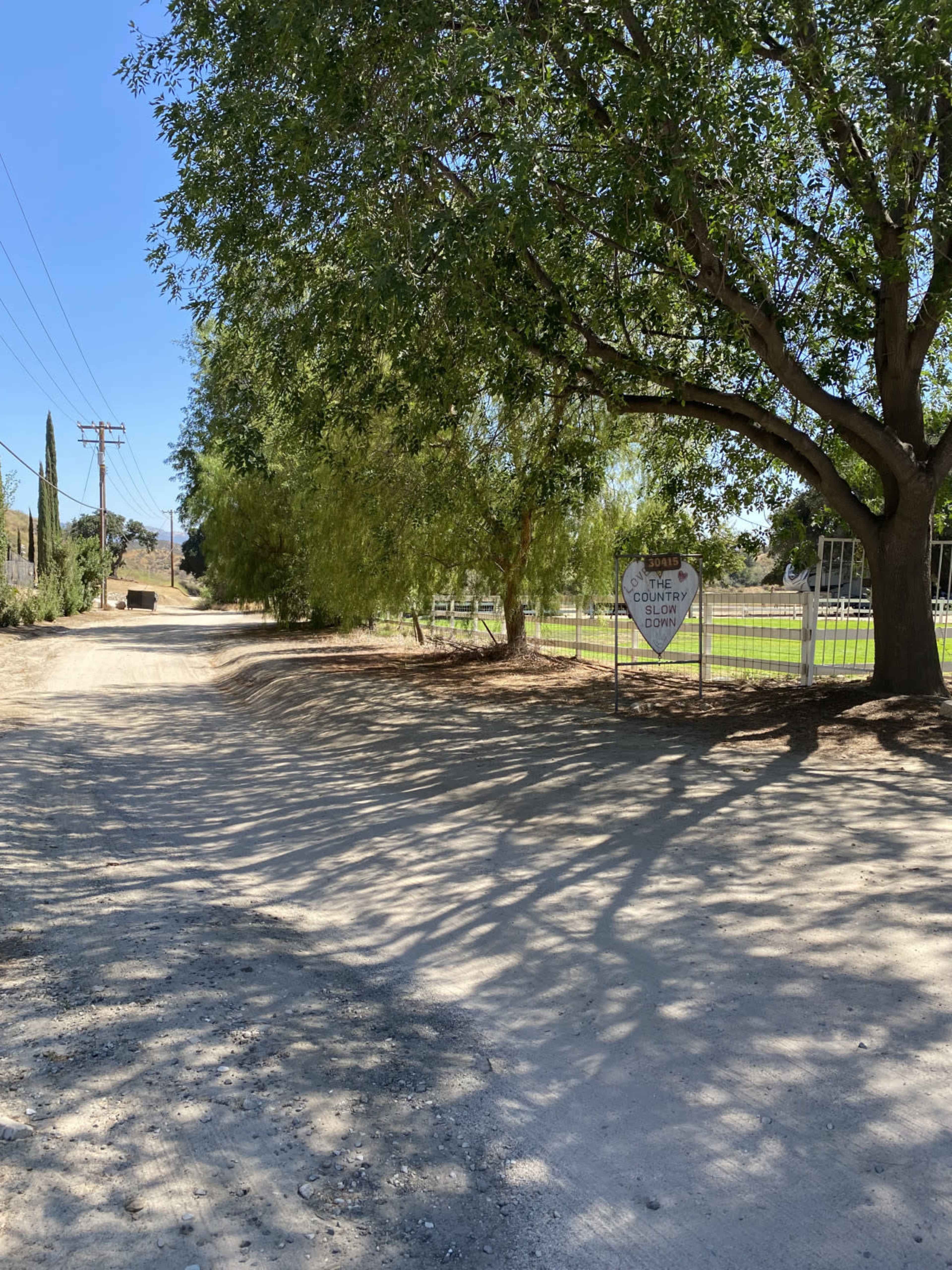 A dirt road lined with trees leads to a sign that indicates the presence of a county park.