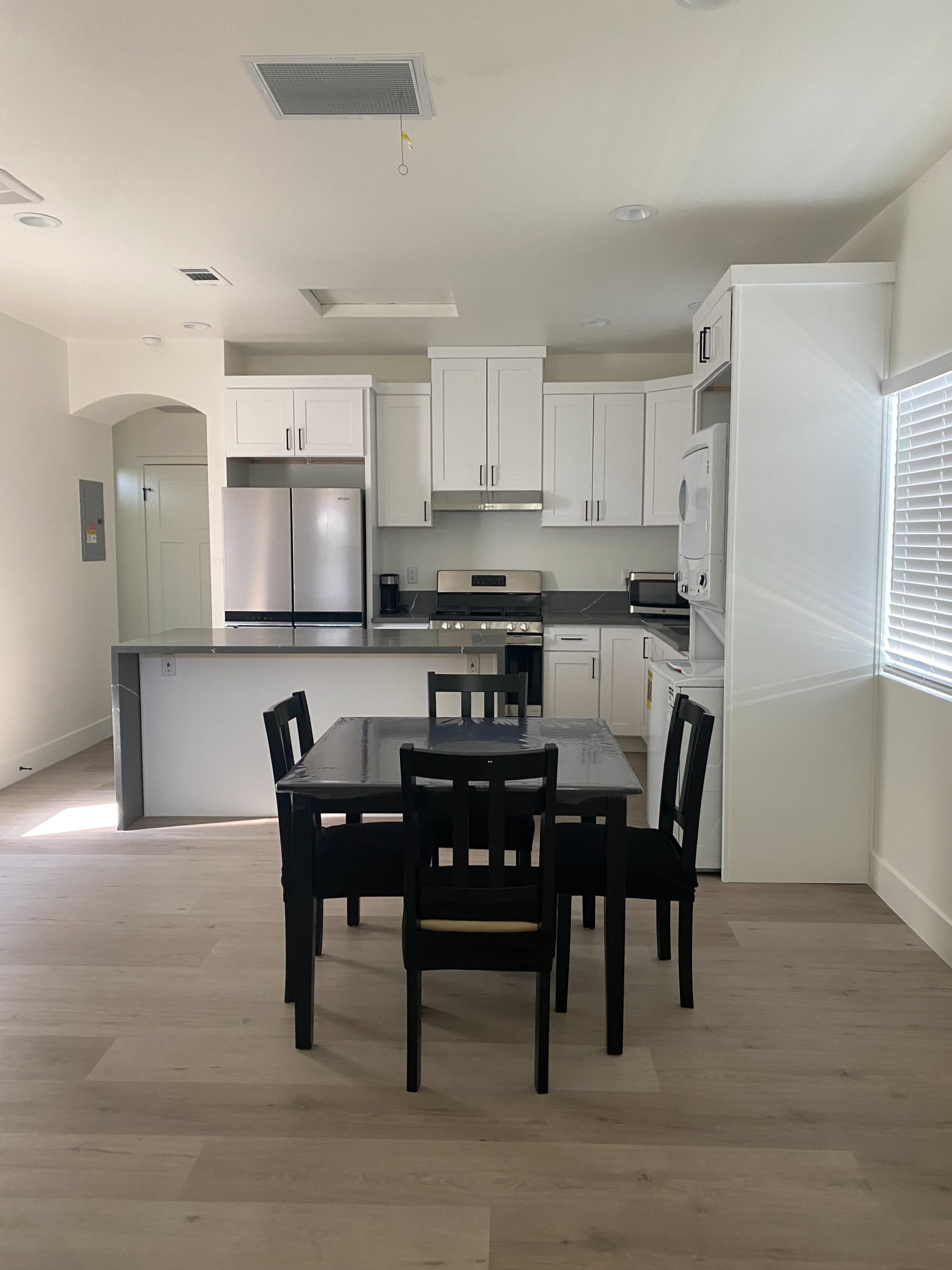 The image shows a modern kitchen with white cabinets, stainless steel appliances, and a black dining table with four chairs in the center.