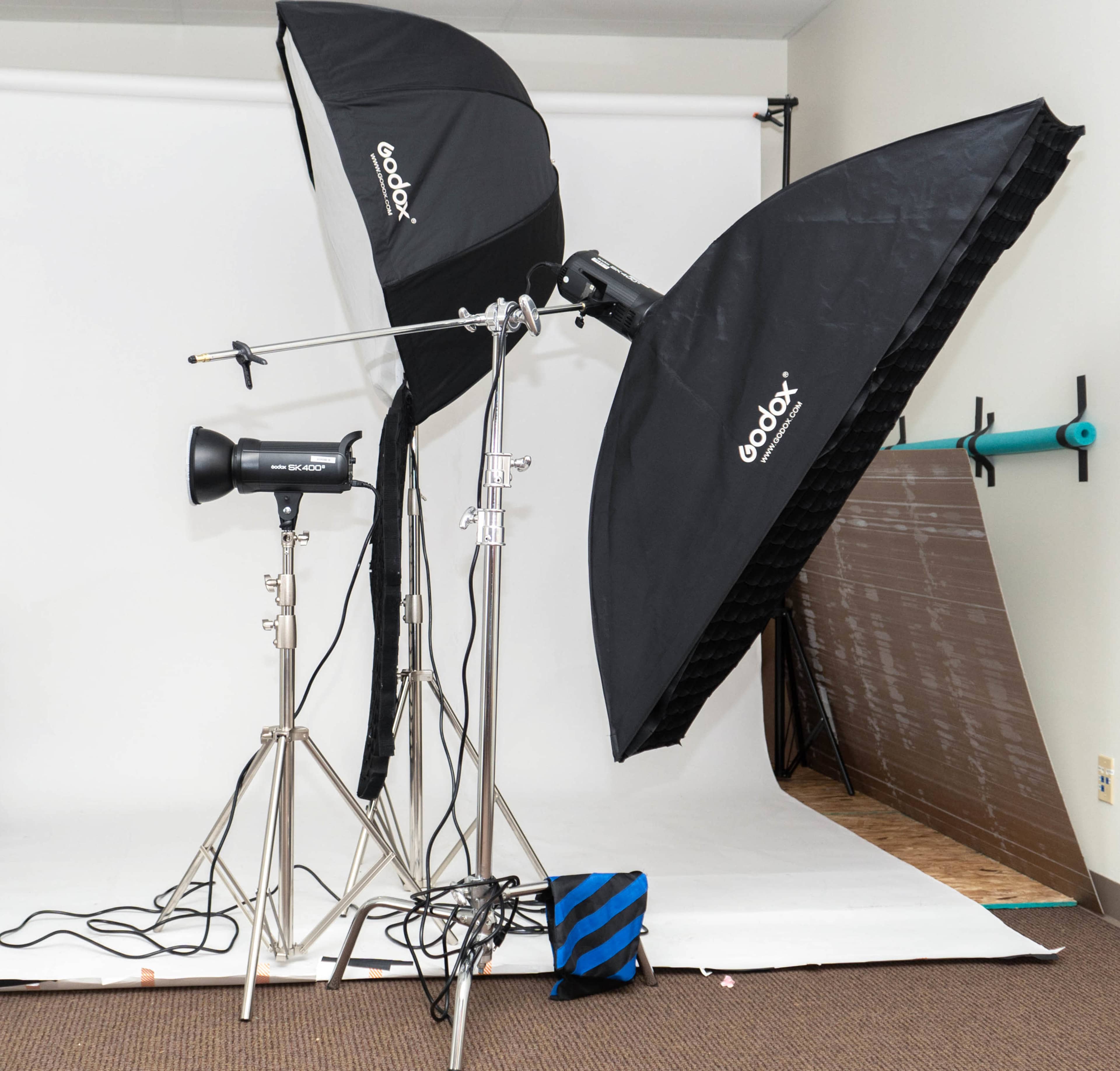The image shows a photography setup featuring two Godox softboxes mounted on light stands, along with a strobe light, all positioned in front of a plain white backdrop.