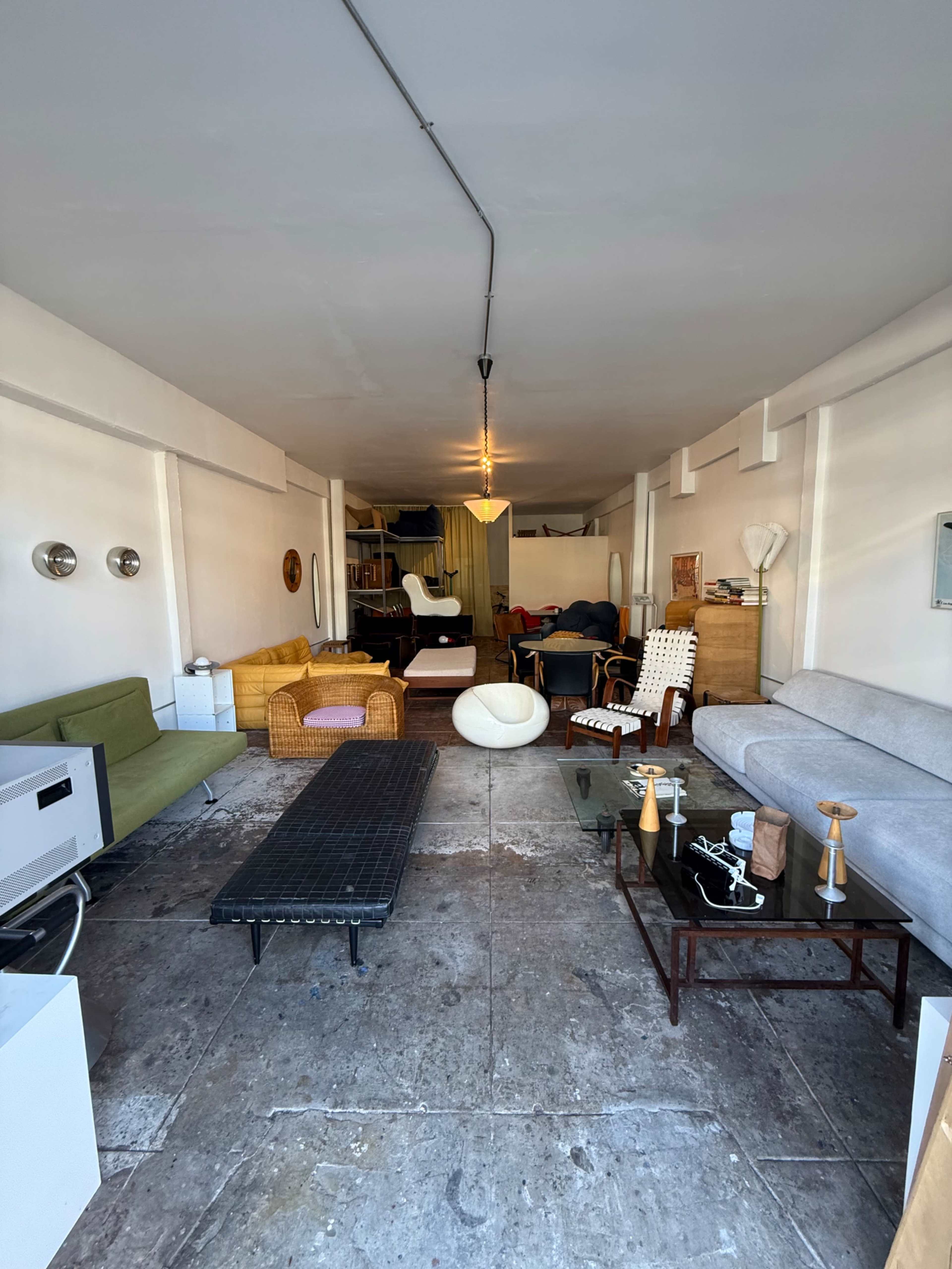 The image shows a long, narrow room furnished with various sofas, chairs, and tables arranged along the walls.