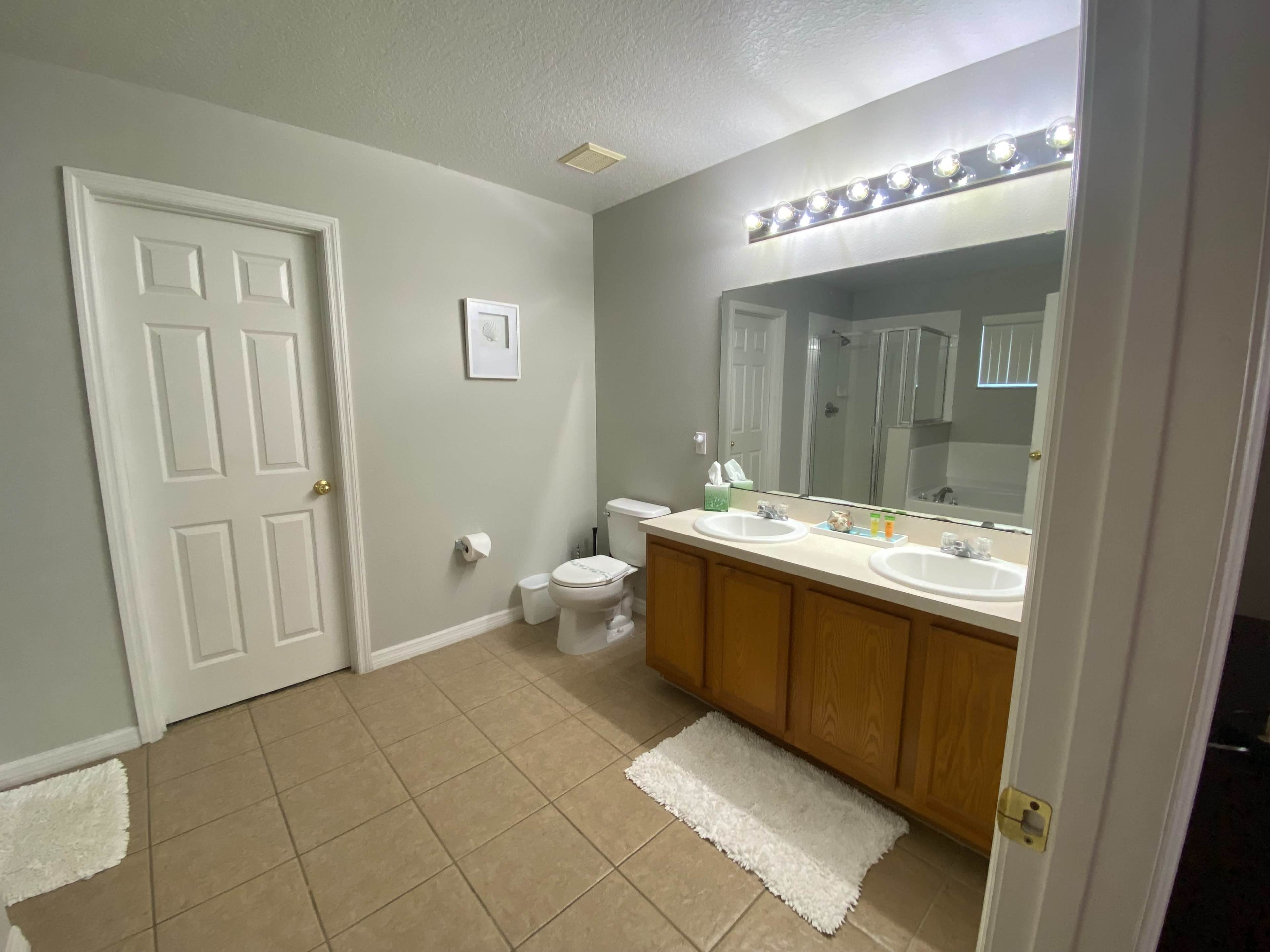 A spacious bathroom with dual sinks, a large mirror, and beige tile flooring.