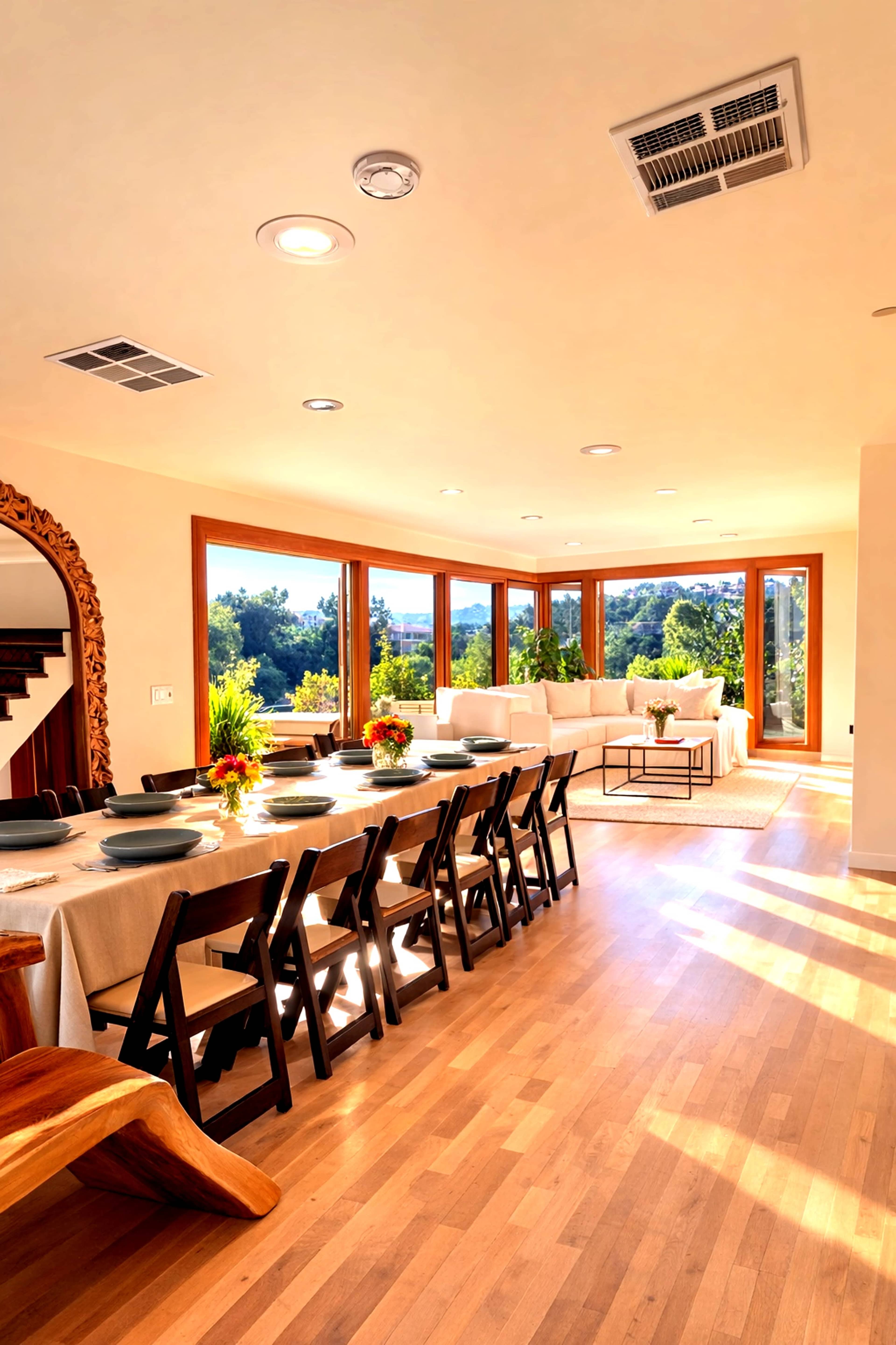A spacious dining area features a long table with chairs, large windows offering views of the outdoors, and a cozy seating arrangement nearby.
