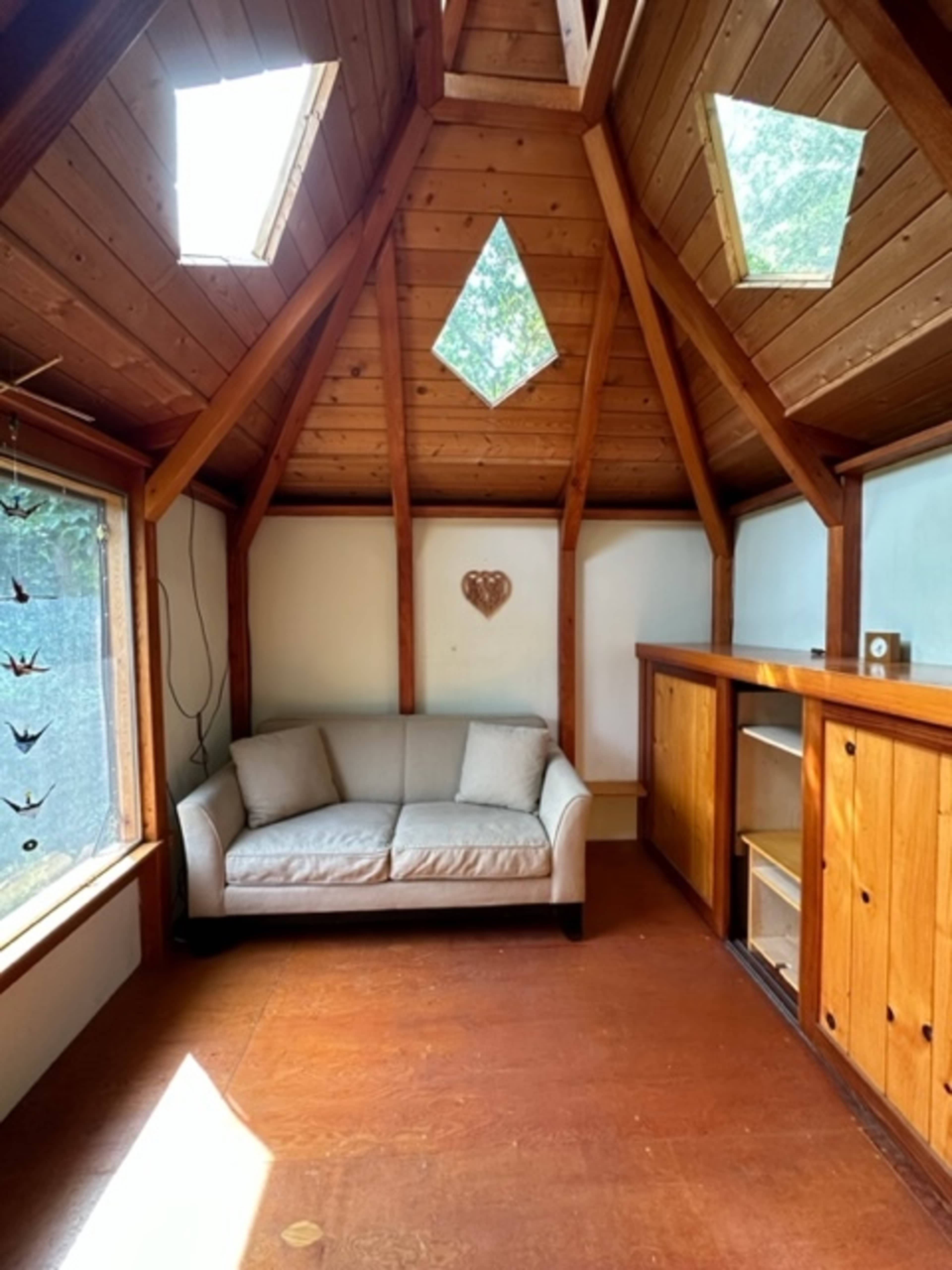 The interior of a small wooden structure features a light-colored sofa and a built-in wooden cabinet, with diamond-shaped windows overhead.