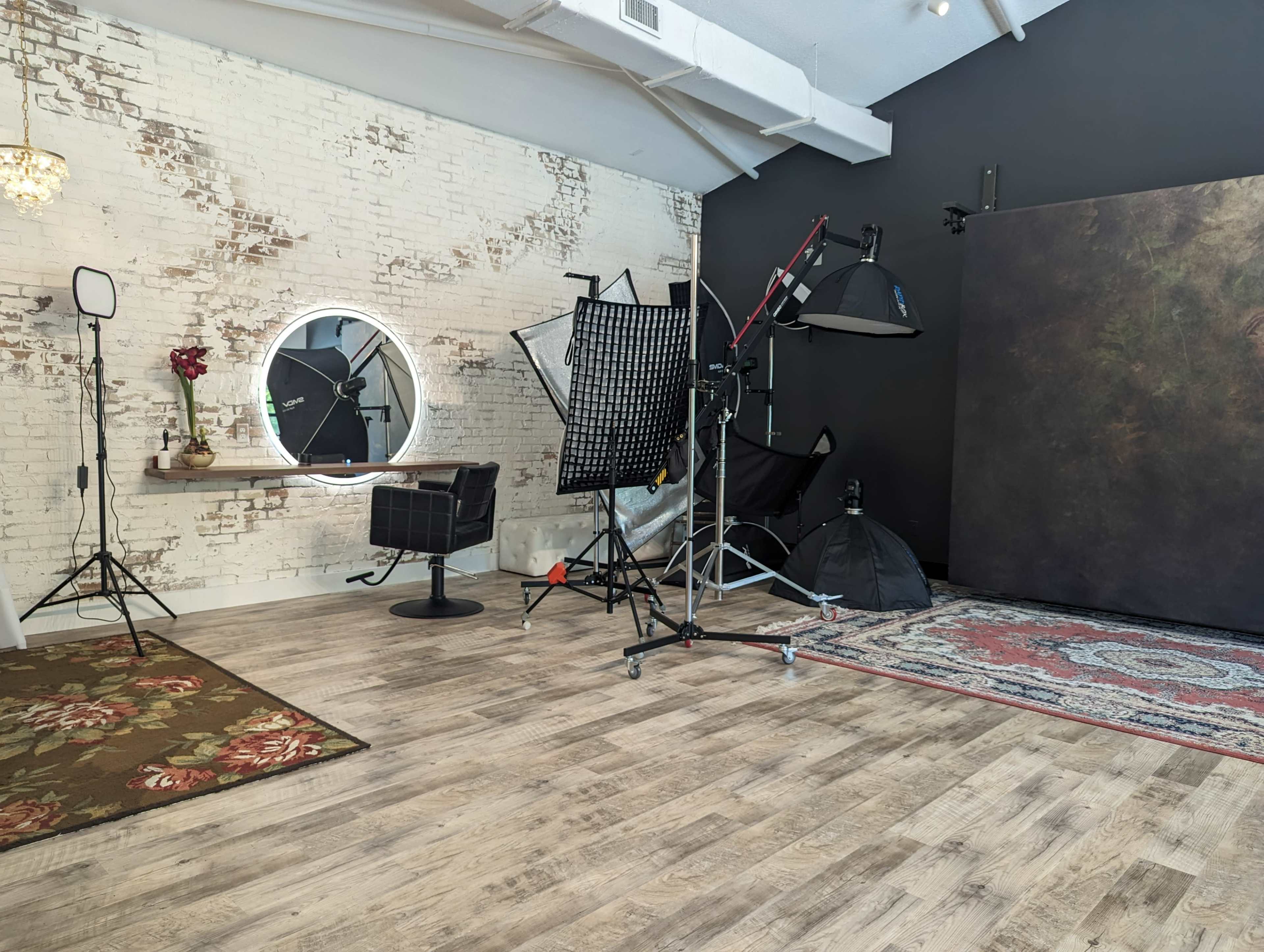 A photography studio with a wooden floor, a backdrop, softboxes, a mirror, and a large floral rug.