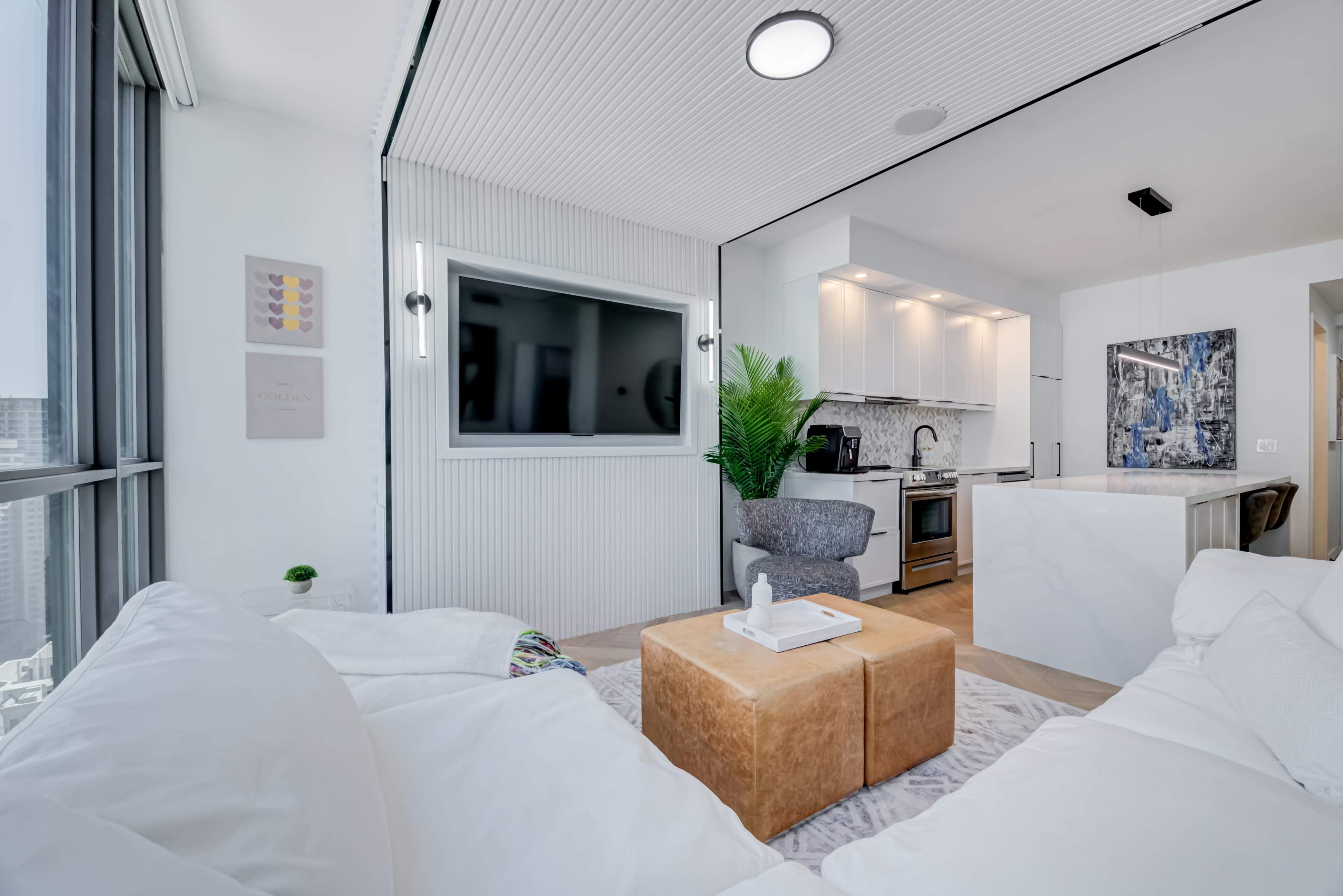 The image shows a modern living space with a white sectional sofa, a marble coffee table, and a kitchen in the background featuring white cabinets and a flat-screen TV on the wall.