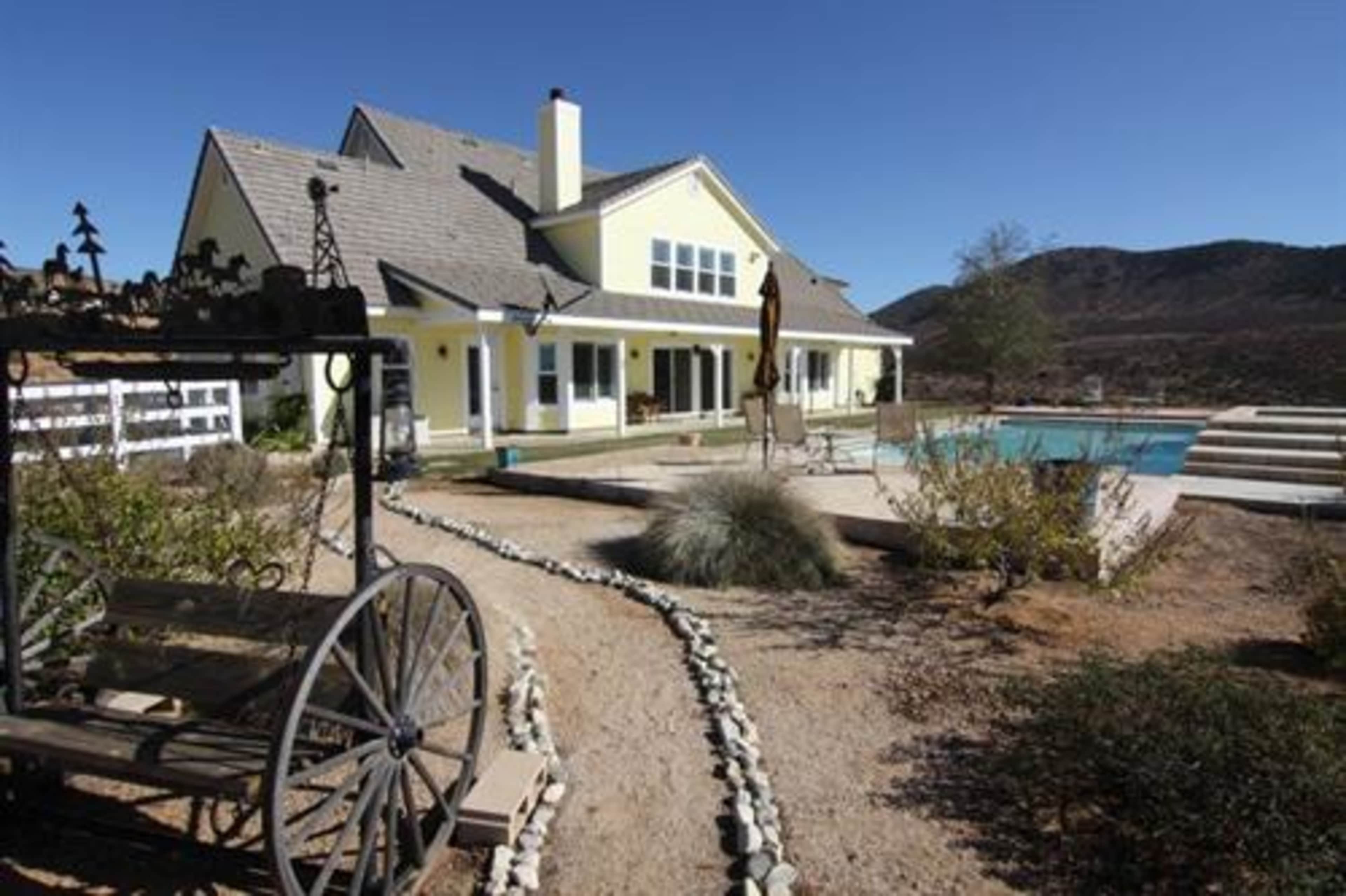 A large yellow house with a pool and a path made of stones in a desert landscape.