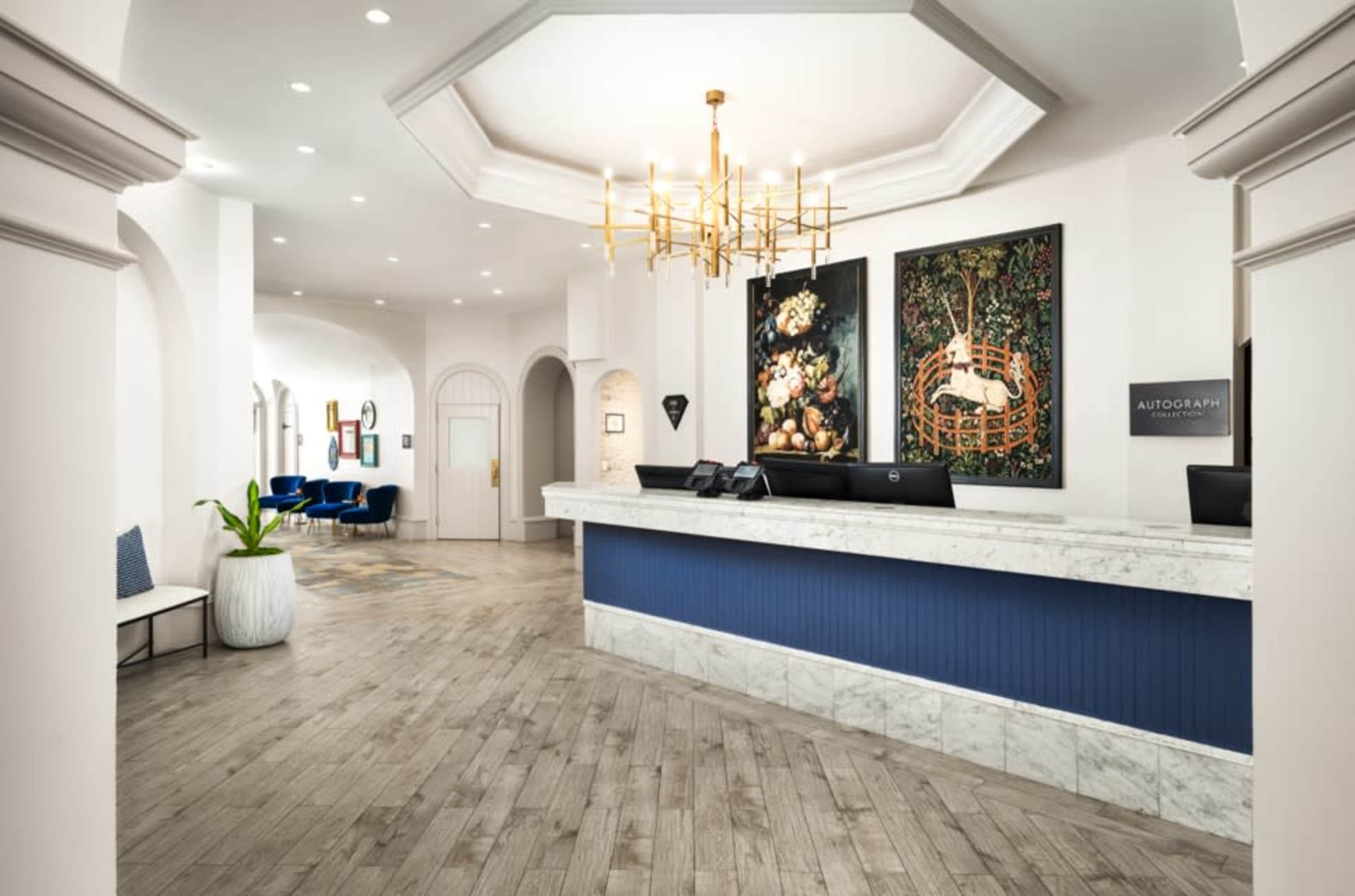 The image shows a hotel reception area featuring a marble-fronted desk, decorative artwork on the walls, and modern seating arrangements.