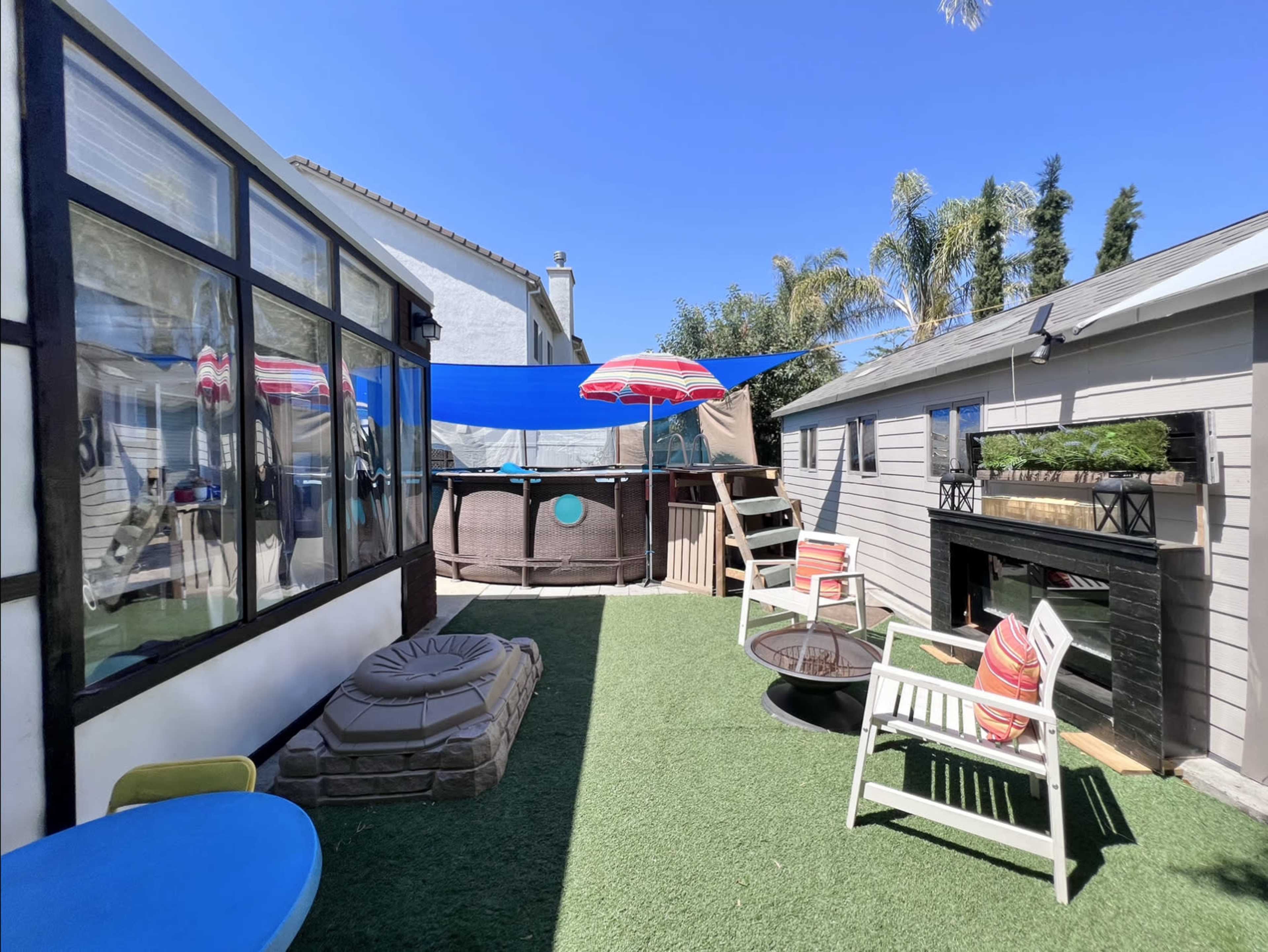 A backyard area featuring a round pool, lounge chairs, an umbrella, and artificial grass.