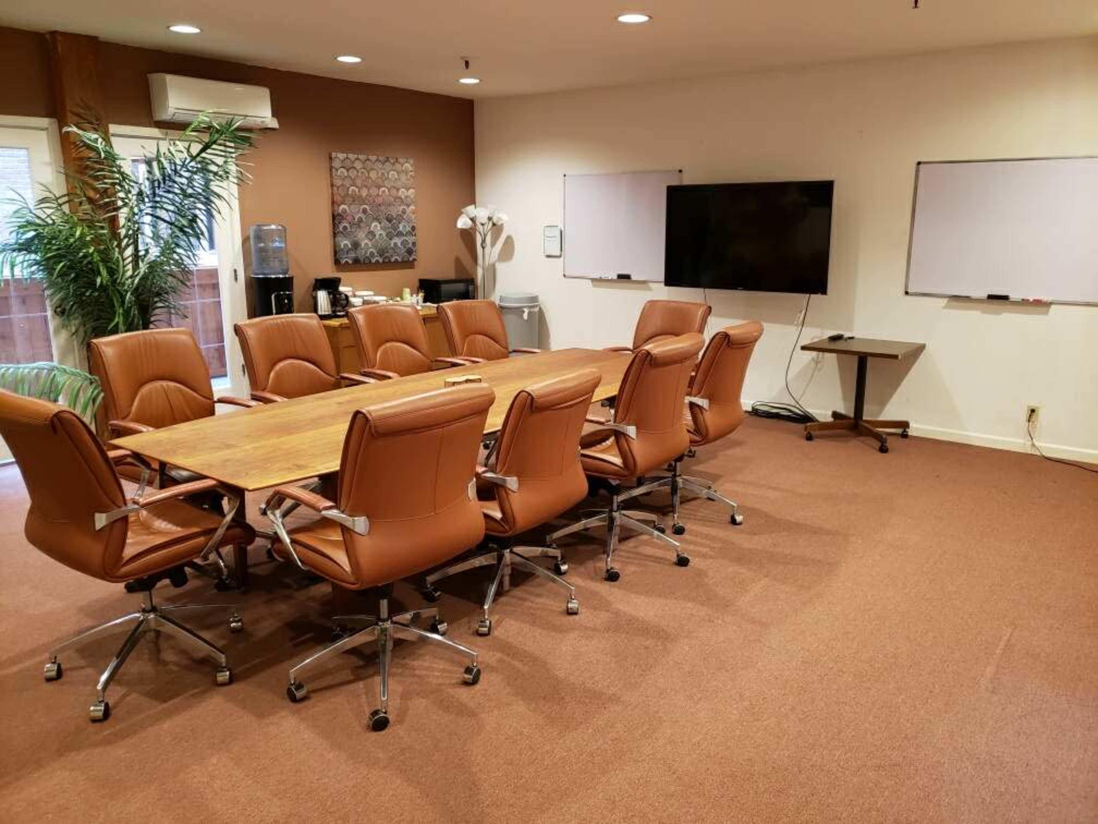 A conference room with a large wooden table surrounded by twelve brown leather chairs, two whiteboards on the walls, and a TV monitor.