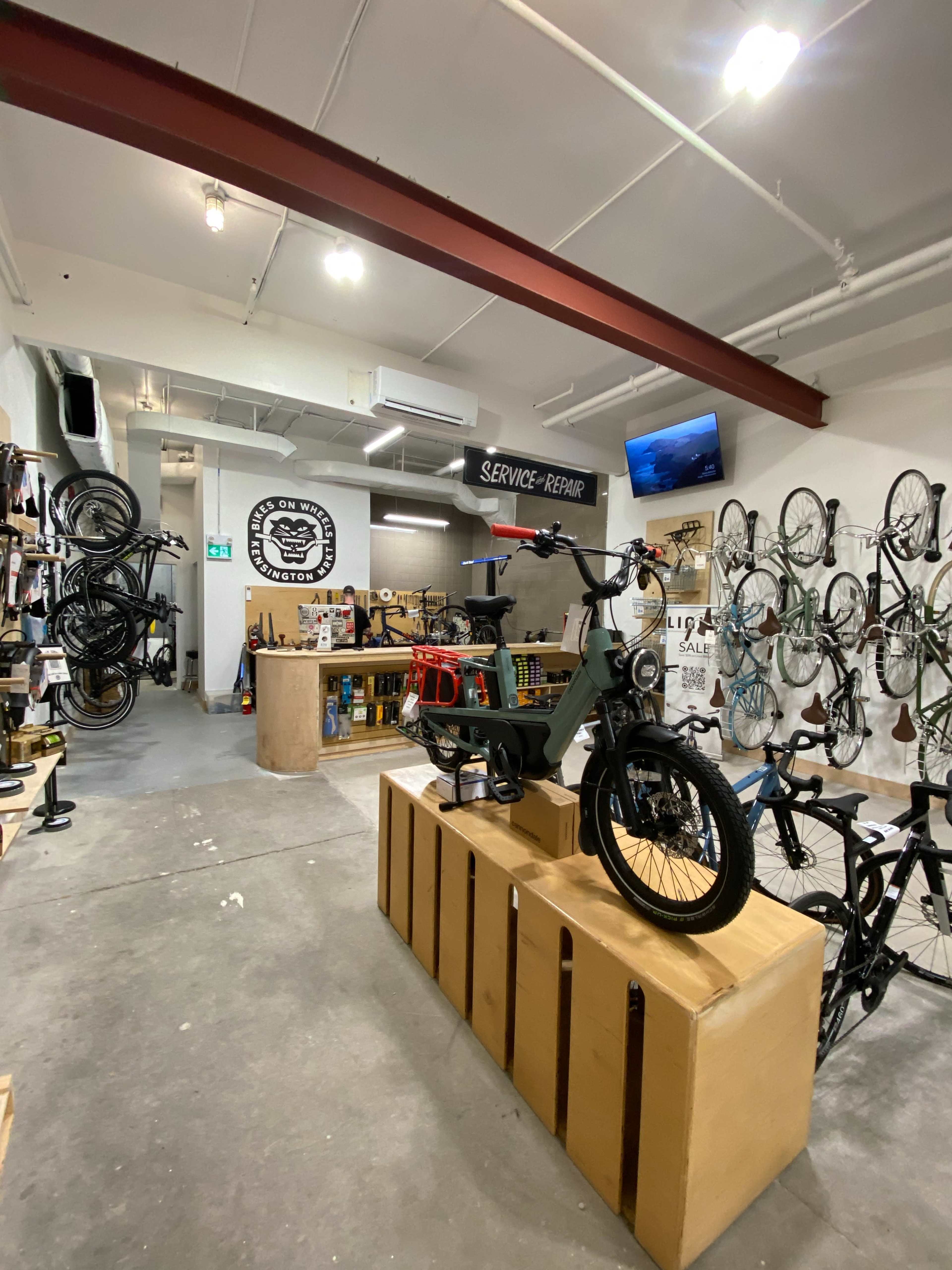The image shows an indoor bike shop with bicycles displayed on the walls and a large bike prominently featured on a wooden platform in the center.
